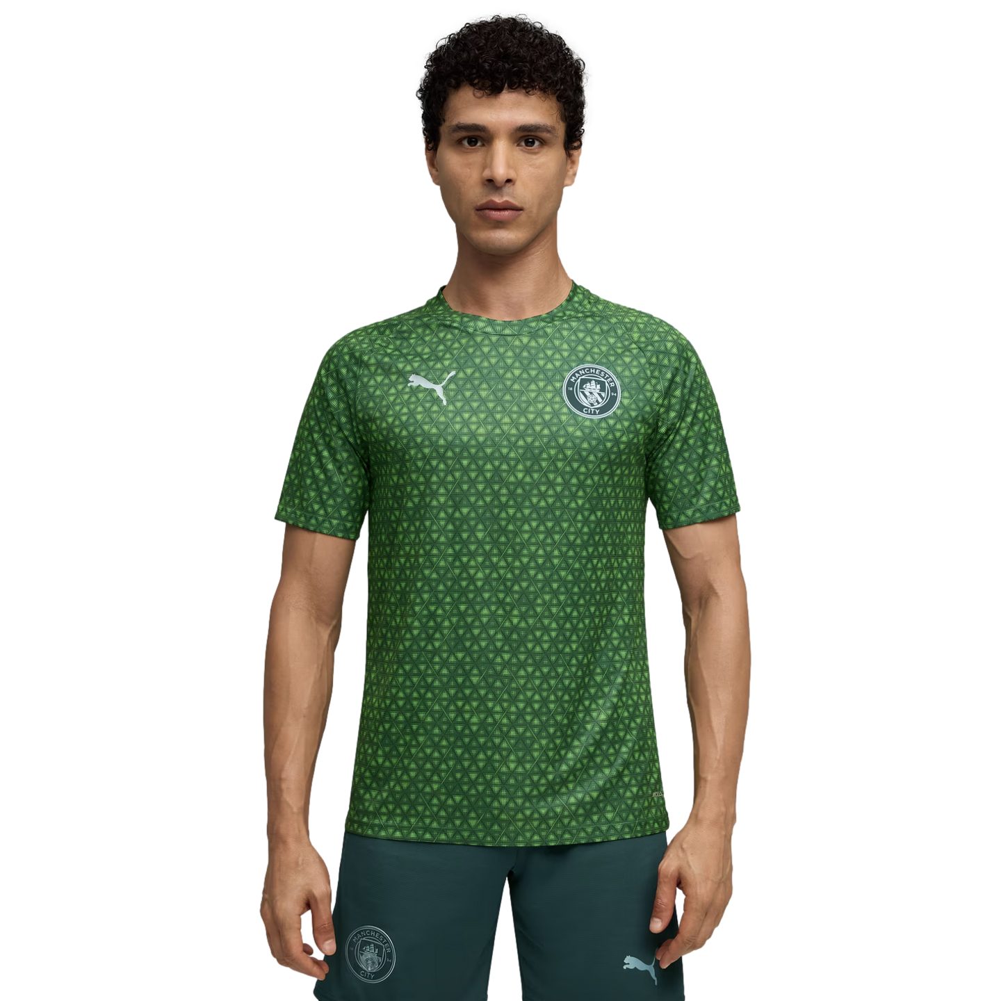 A man wearing a green, patterned Manchester City training jersey and dark green shorts.