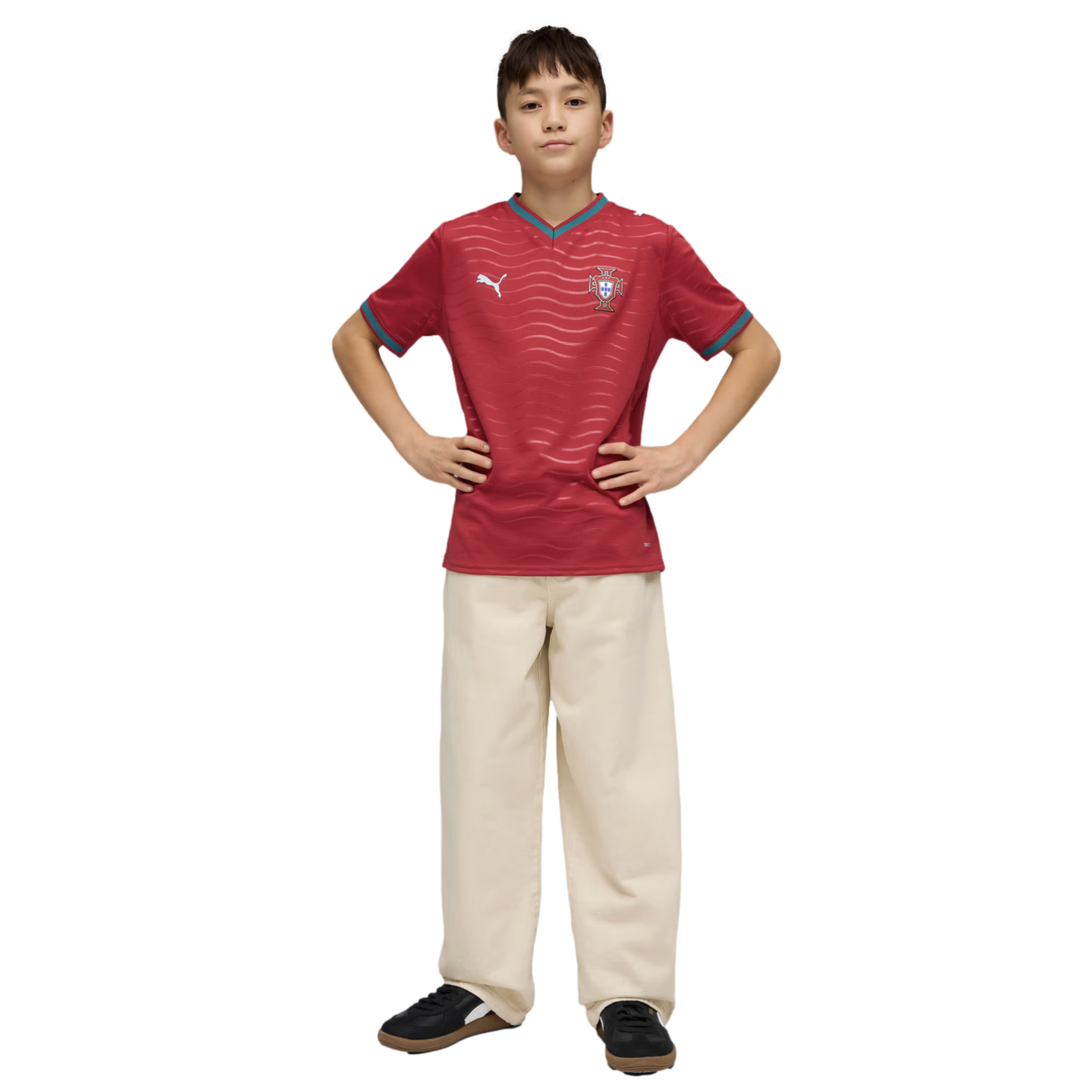 A boy posing in a red wavy-patterned sports jersey and cream-colored wide-leg trousers with his hands on his hips against a black background.