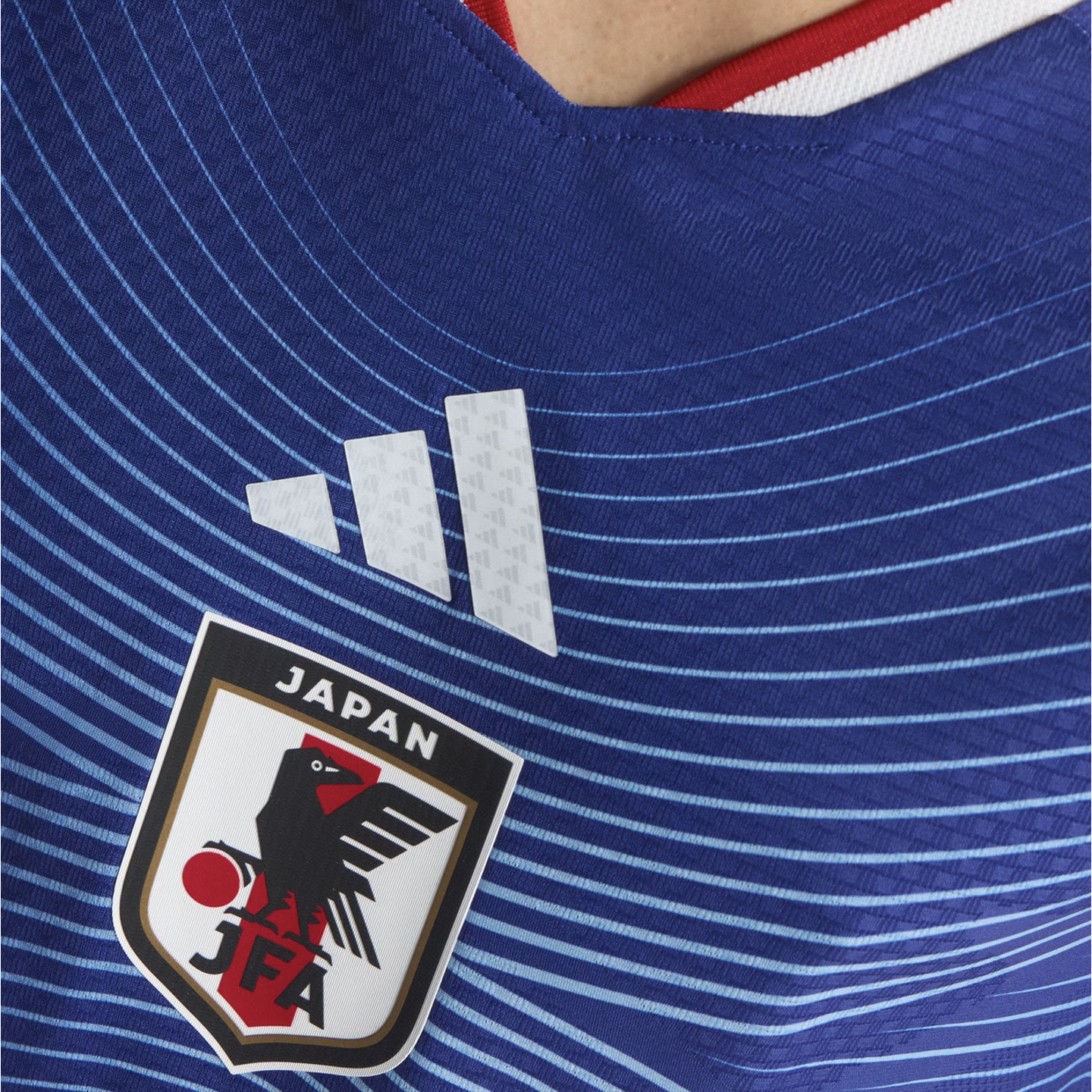 Close-up of a blue Japan national soccer team jersey featuring horizontal stripes, the white Adidas logo, and the JFA crest.