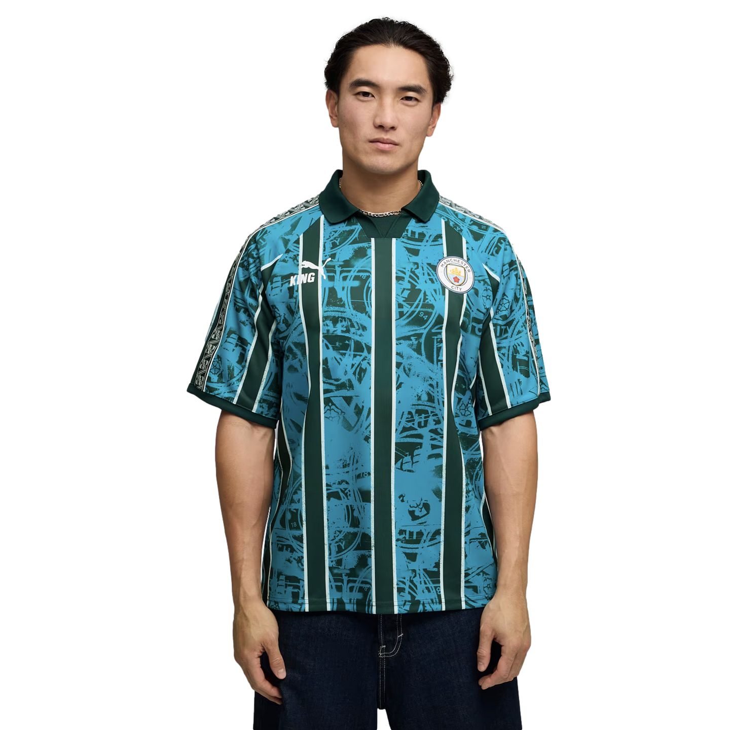 Man wearing a teal and dark green patterned Manchester City soccer jersey with vertical stripes, posed against a plain black background.