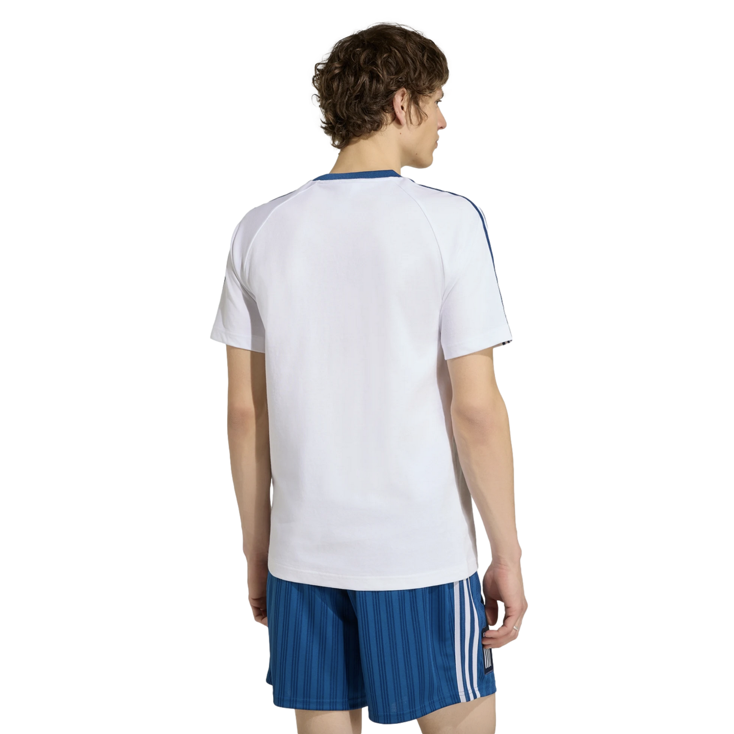 Rear view of a man in a white t-shirt with blue trim and blue striped athletic shorts against a black background.