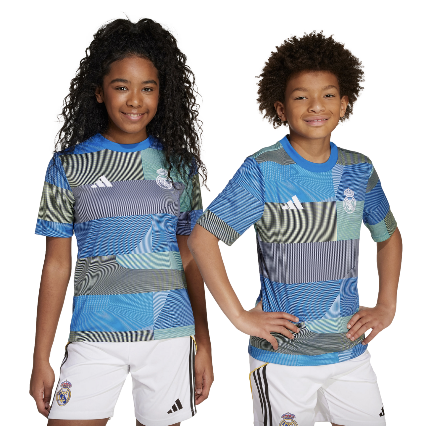 Two children smile while posing in matching blue and teal geometric-patterned Real Madrid soccer jerseys and white shorts.