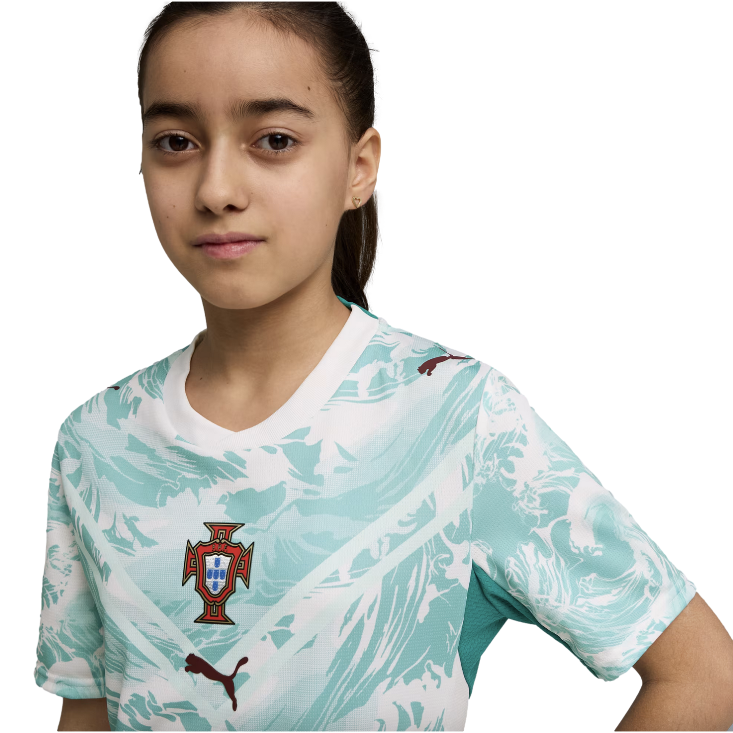 A young girl with dark hair tied back wears a white and teal patterned Portugal national football team jersey with the FPF crest and dark red Puma logos. She looks directly at the camera against a solid black background.