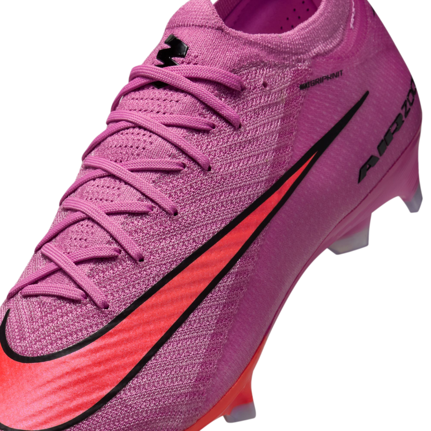 Close-up of a pink Nike soccer cleat featuring a textured Gripknit upper, matching laces, and a bold red swoosh with black outline against a dark background.