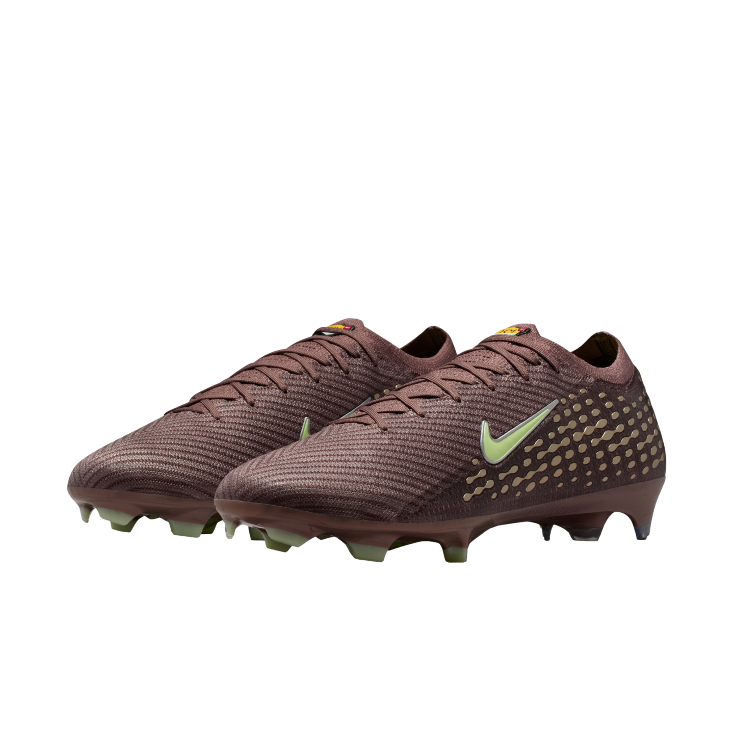 A pair of dark reddish-brown Nike soccer cleats with light green swooshes and studs, featuring a golden dot pattern, against a solid black background.