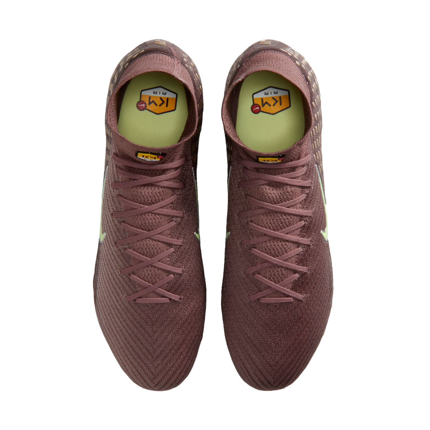 Top-down view of maroon Nike soccer cleats with neon yellow insoles and Kylian Mbappé "KM" branding, set against a solid black background.