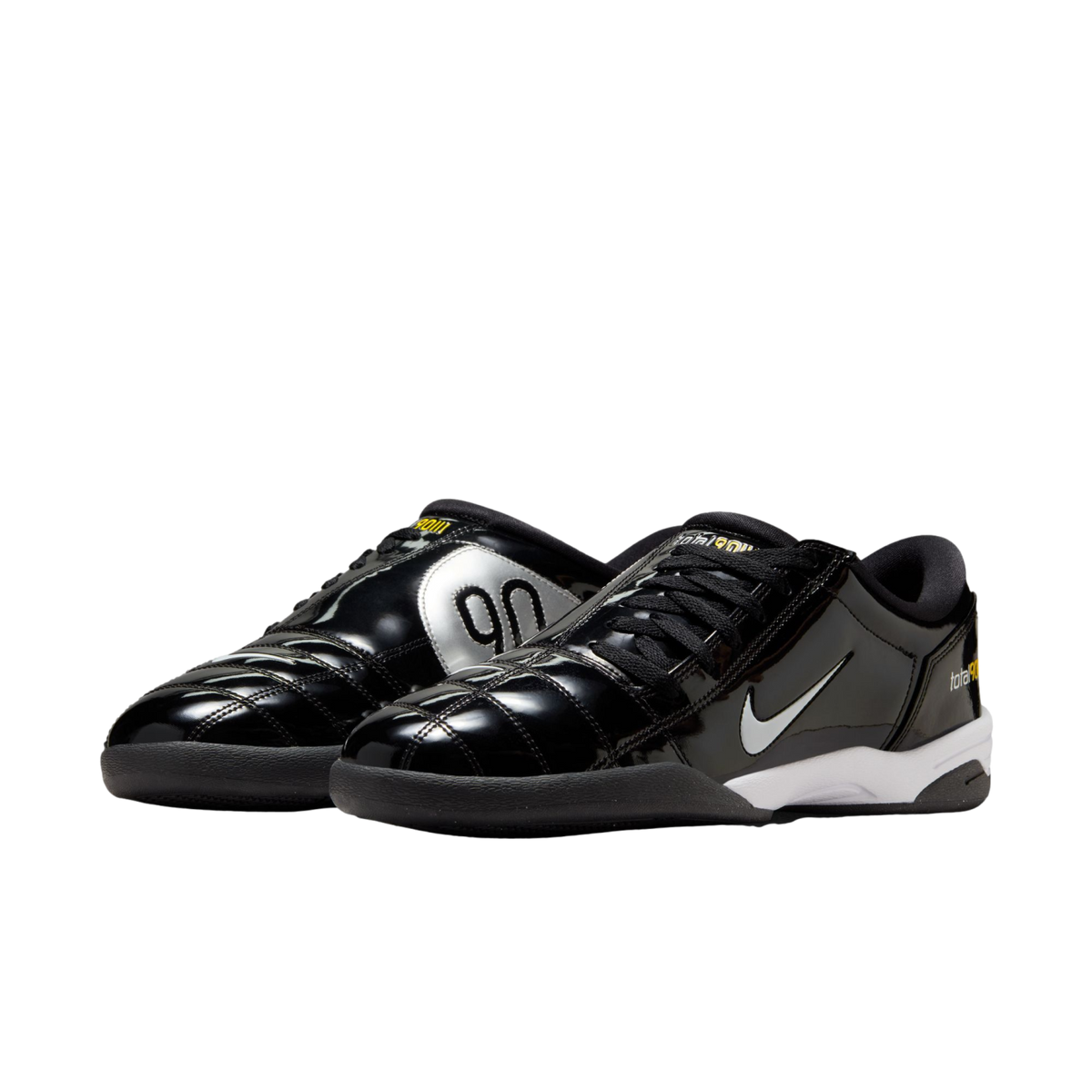 A pair of glossy black Nike Total 90 indoor soccer shoes with silver "90" branding, white swooshes, and yellow accents, shown against a white background.