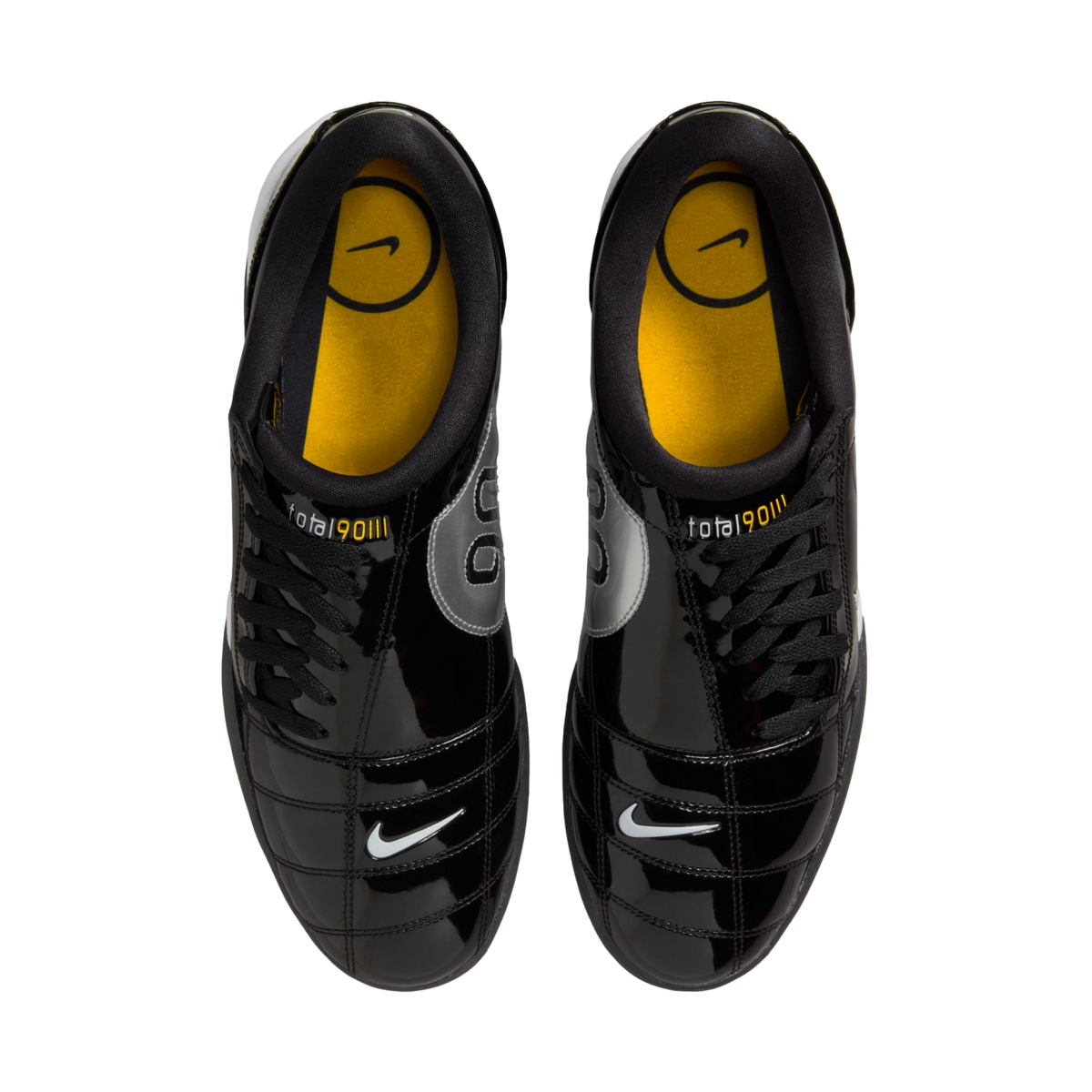 Top-down view of shiny black Nike Total 90 III soccer shoes with yellow insoles and small white swooshes on the toes, against a white background.