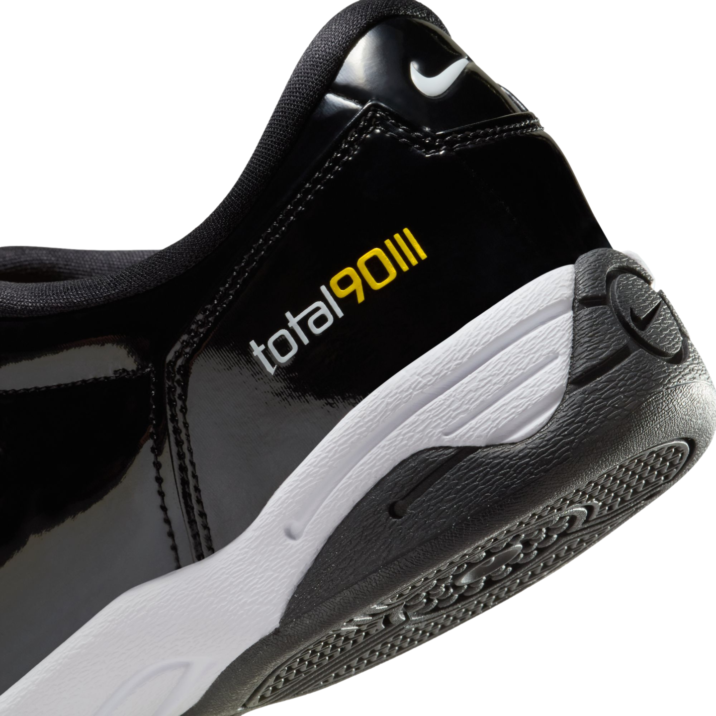 Close-up of the heel of a black patent leather Nike Total 90 III shoe with white and yellow branding, a white midsole, and a black textured outsole.