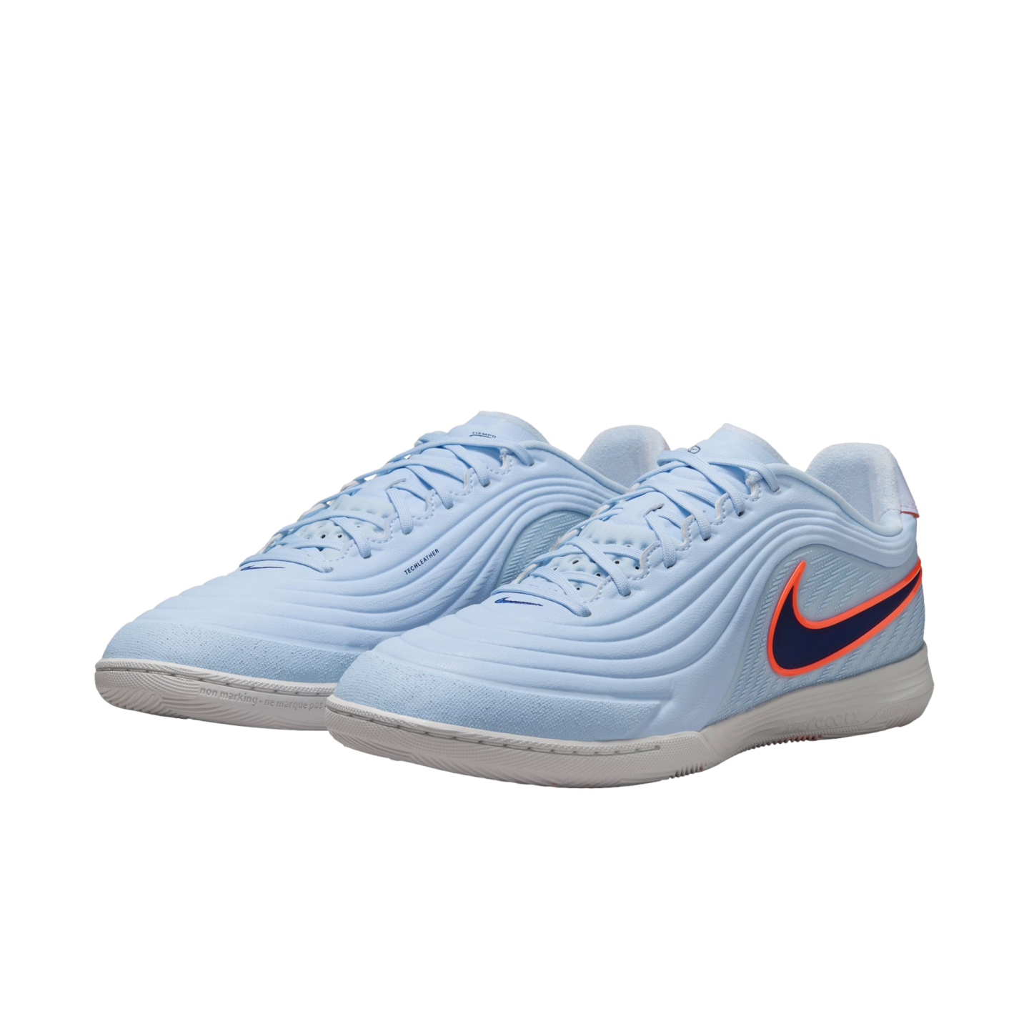 A pair of light blue Nike indoor soccer shoes with a dark blue swoosh outlined in bright orange. The shoes feature a textured, wavy upper design and a white rubber sole, shown against a solid black background.