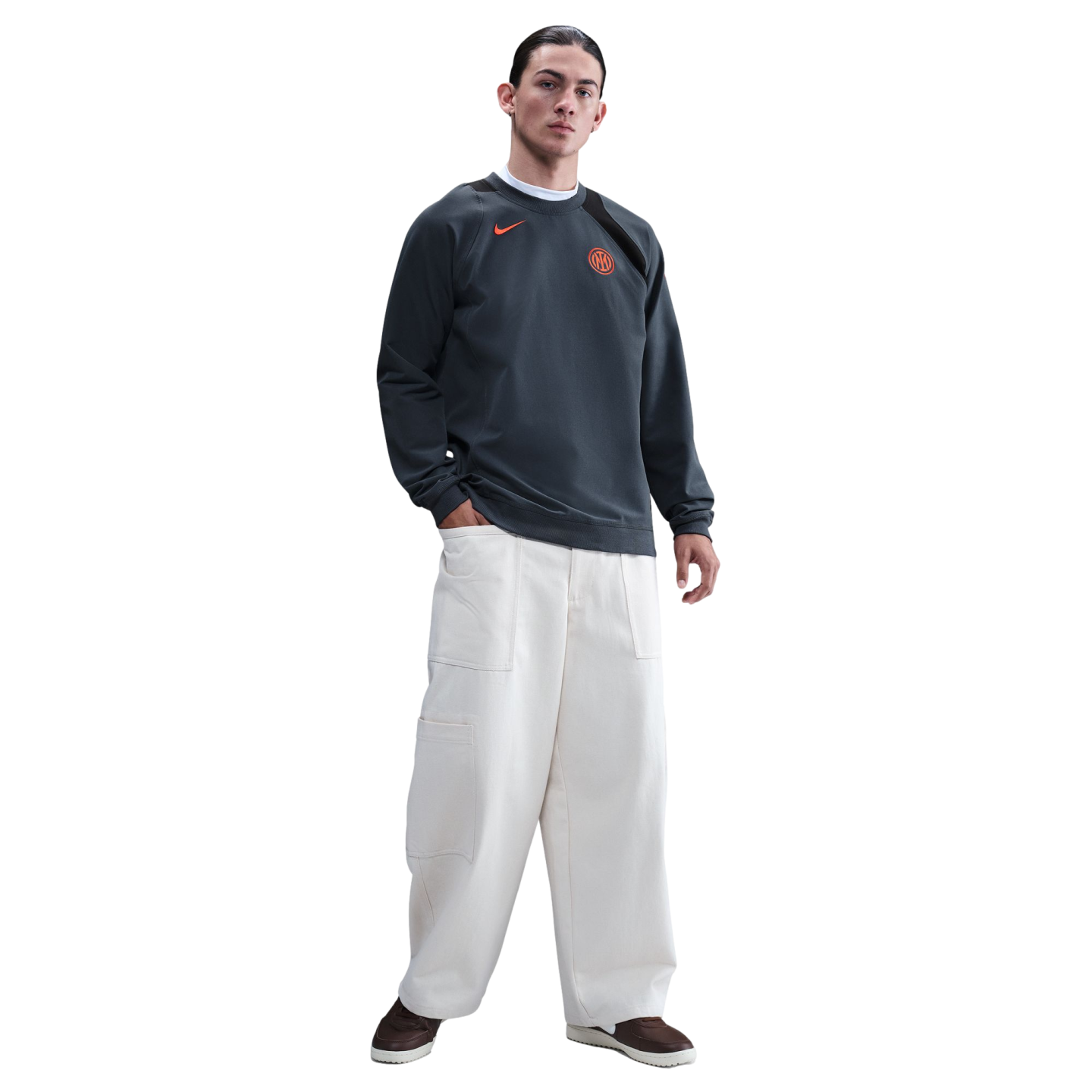 A man wearing a dark grey Inter Milan Nike sweatshirt and wide-leg off-white trousers against a black background.