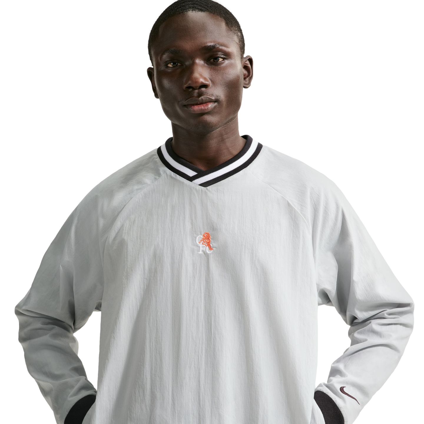 A man in a light grey Nike windbreaker shirt with a striped v-neck and orange lion crest, posing against a black background.