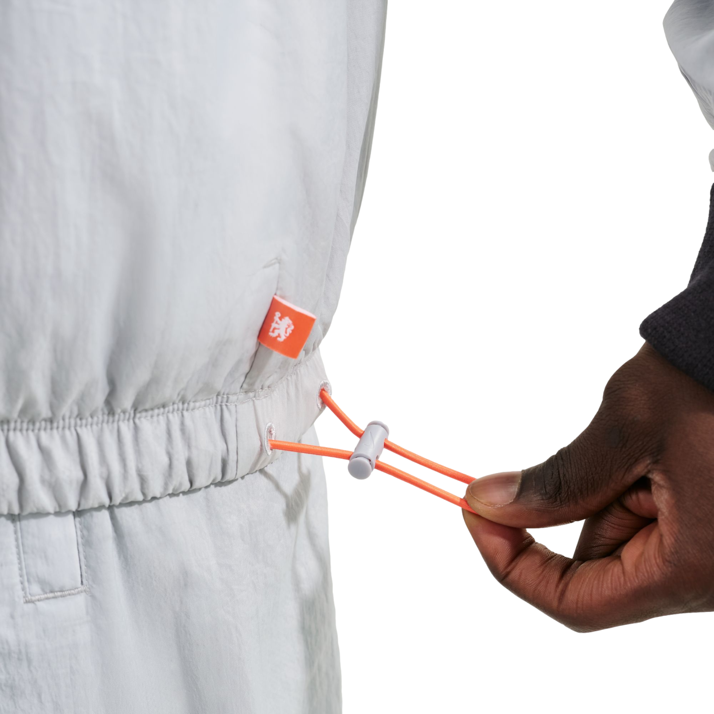 Close-up of a hand pulling an orange drawstring toggle on a light gray elastic waist garment with a small orange logo tag.