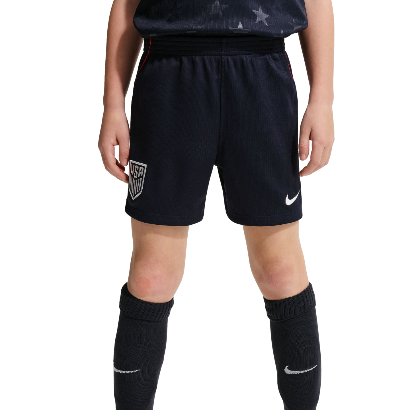 A front-facing view of a youth athlete from the waist down wearing navy blue USA national team soccer shorts and matching knee-high Nike socks against a black background.