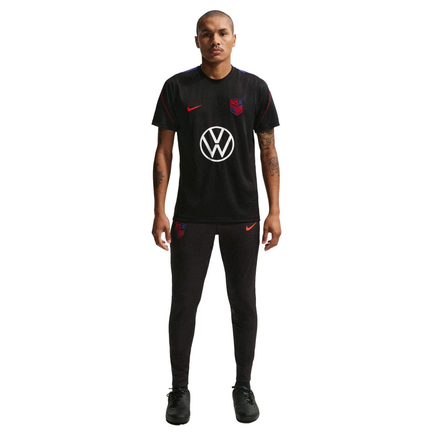 A man stands against a black background wearing a black Nike USA soccer training uniform featuring a large white Volkswagen logo on the shirt.