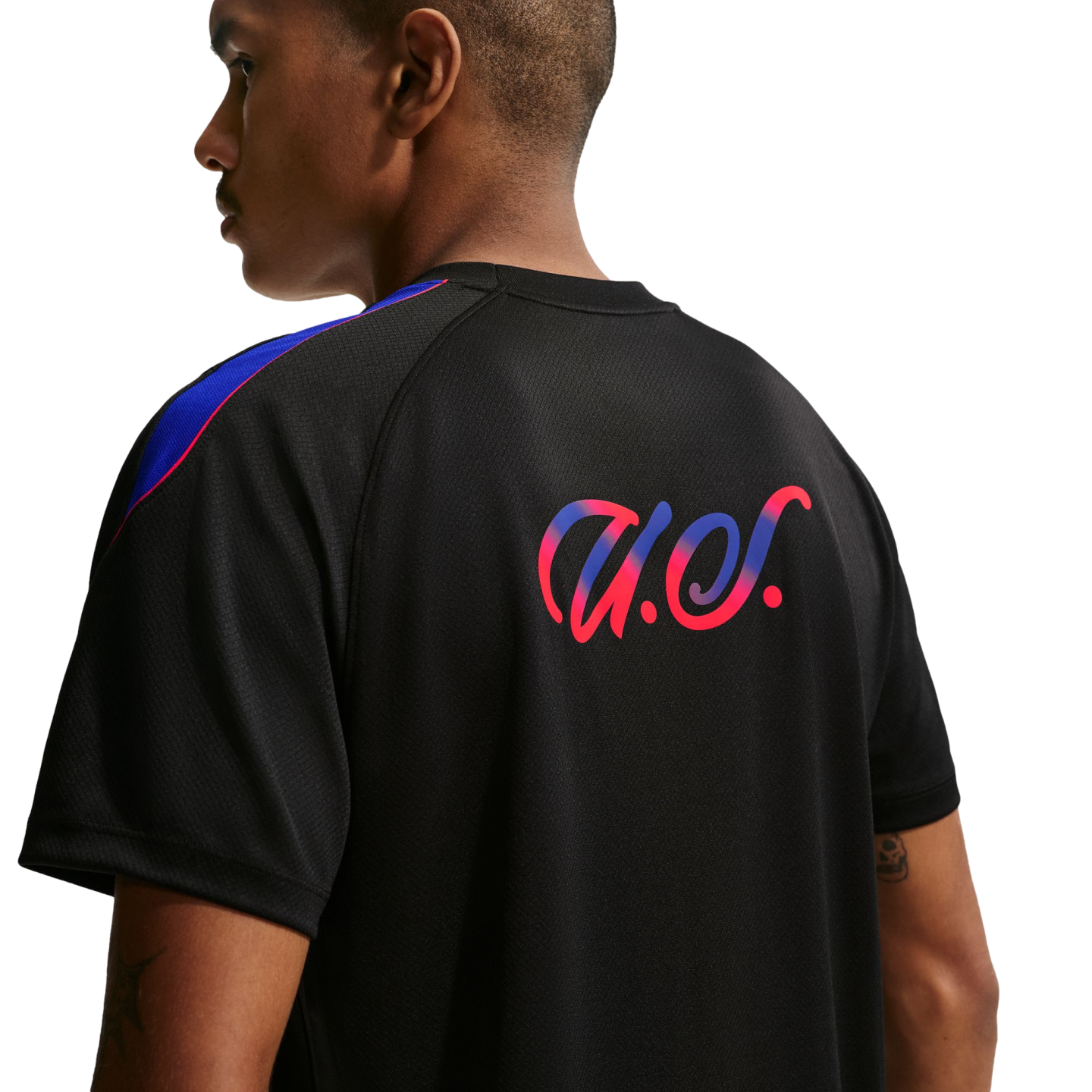 Rear view of a man wearing a black athletic shirt featuring a pink and blue gradient script logo and colorful shoulder stripes.