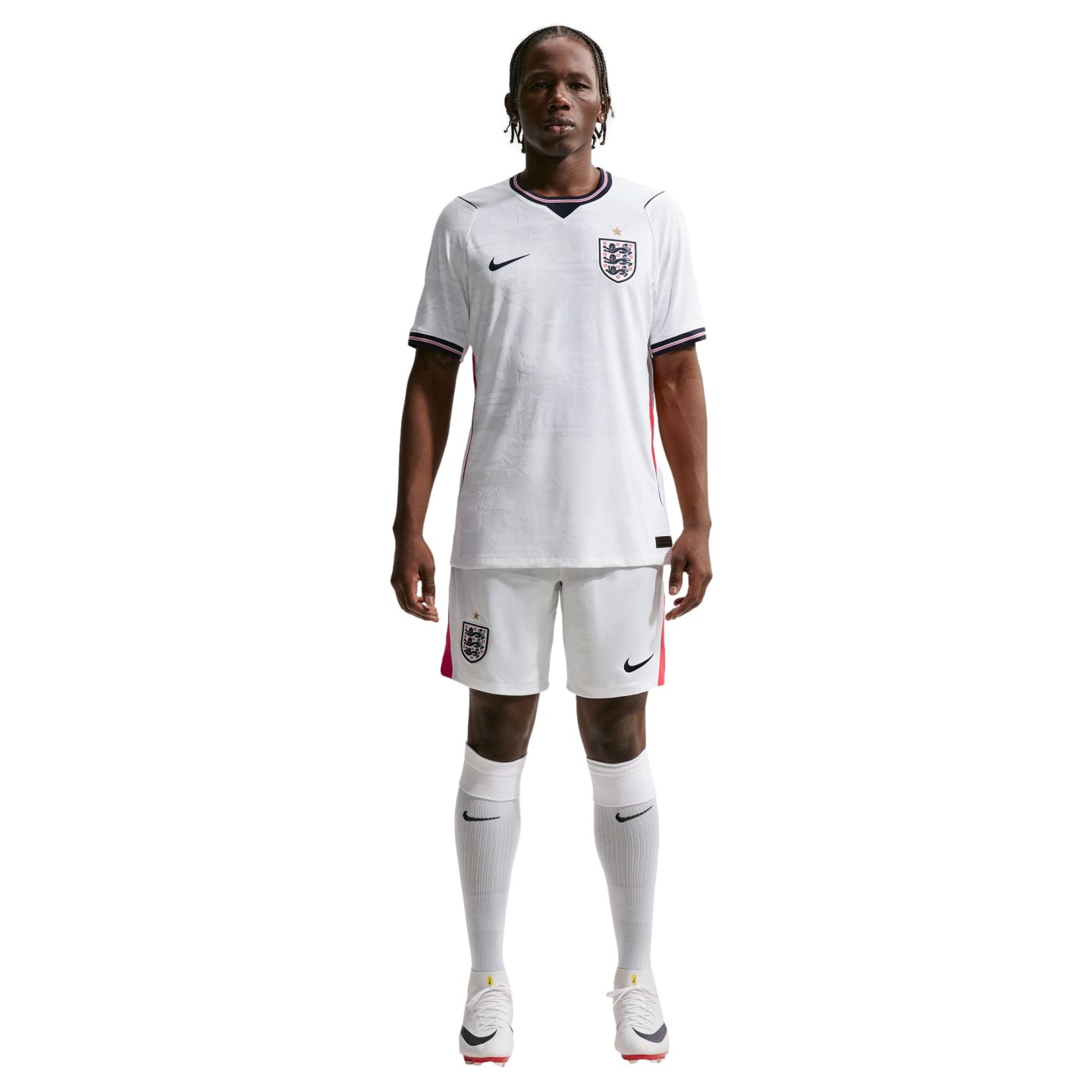 A full-body photograph of a male athlete standing against a solid black background, wearing the white Nike England national team home soccer kit. The kit includes a white jersey and shorts featuring the team's Three Lions crest and Nike logo, paired with 