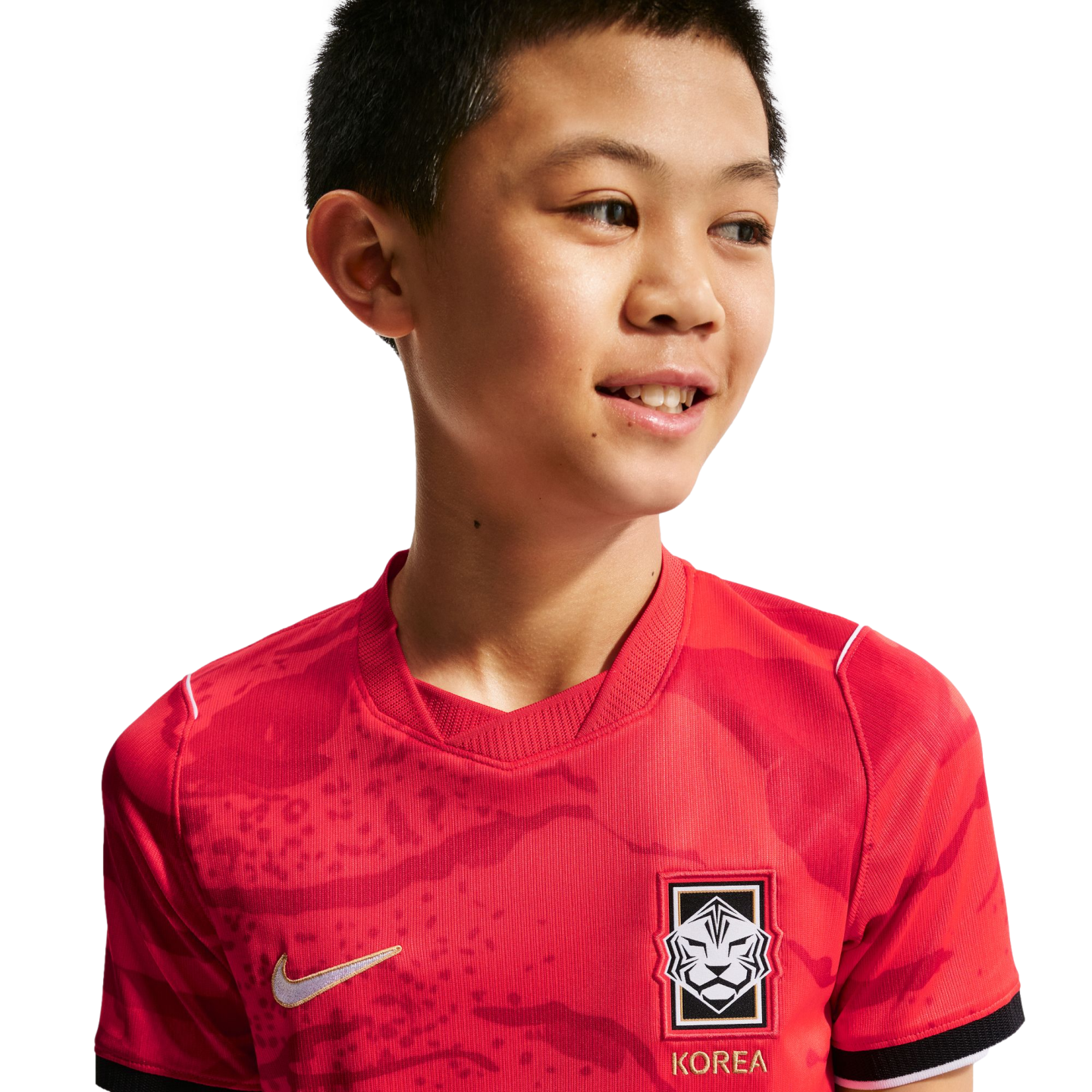 A smiling young boy wearing a red South Korea national football jersey with a subtle tiger pattern, against a solid black background.