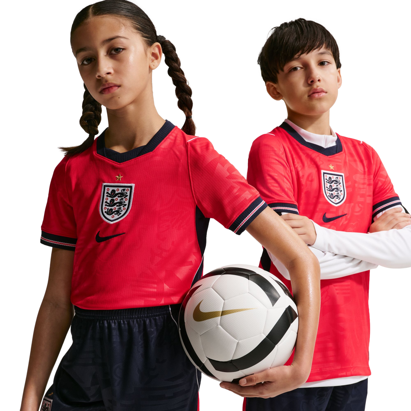 A girl and boy in red England football kits pose against a black background. The girl holds a Nike soccer ball while the boy stands with his arms crossed.