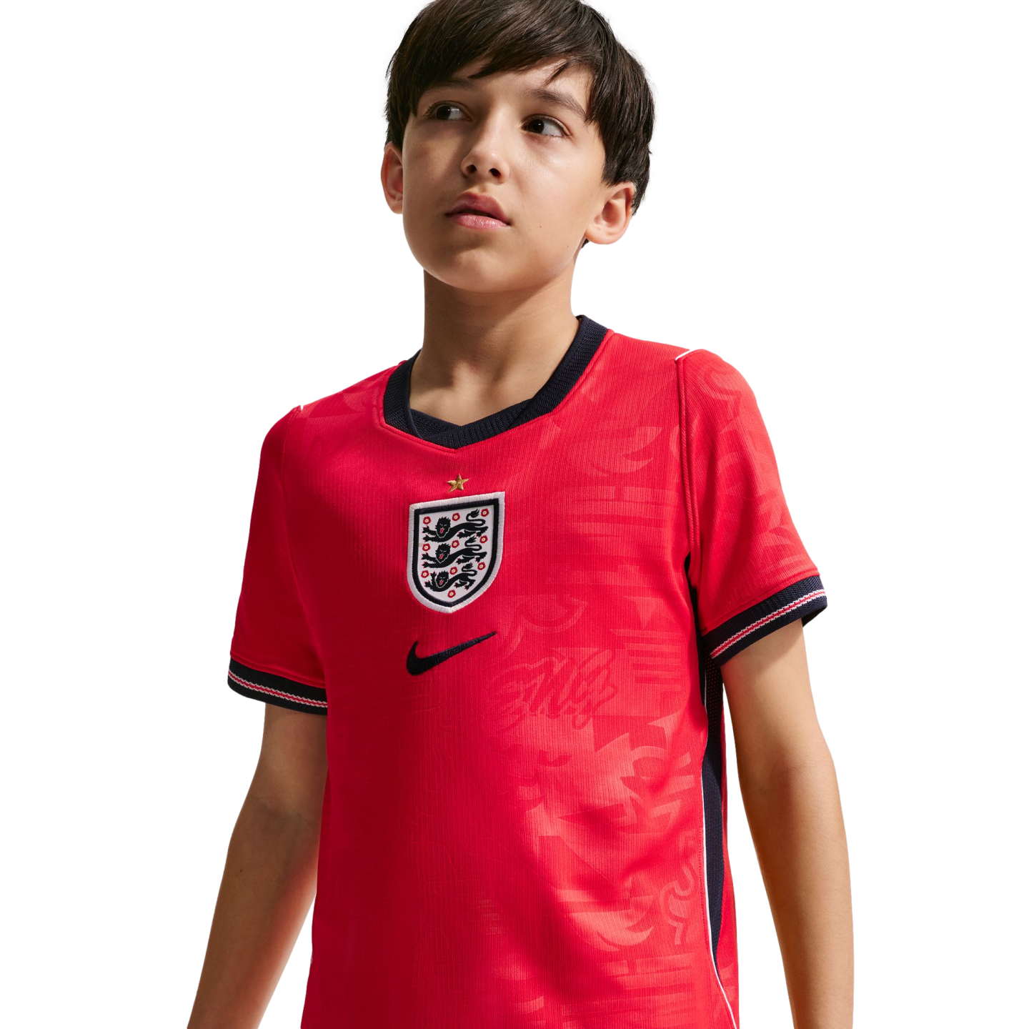 A young boy wearing a red England national football team jersey with the Three Lions crest, looking off-camera against a black background.