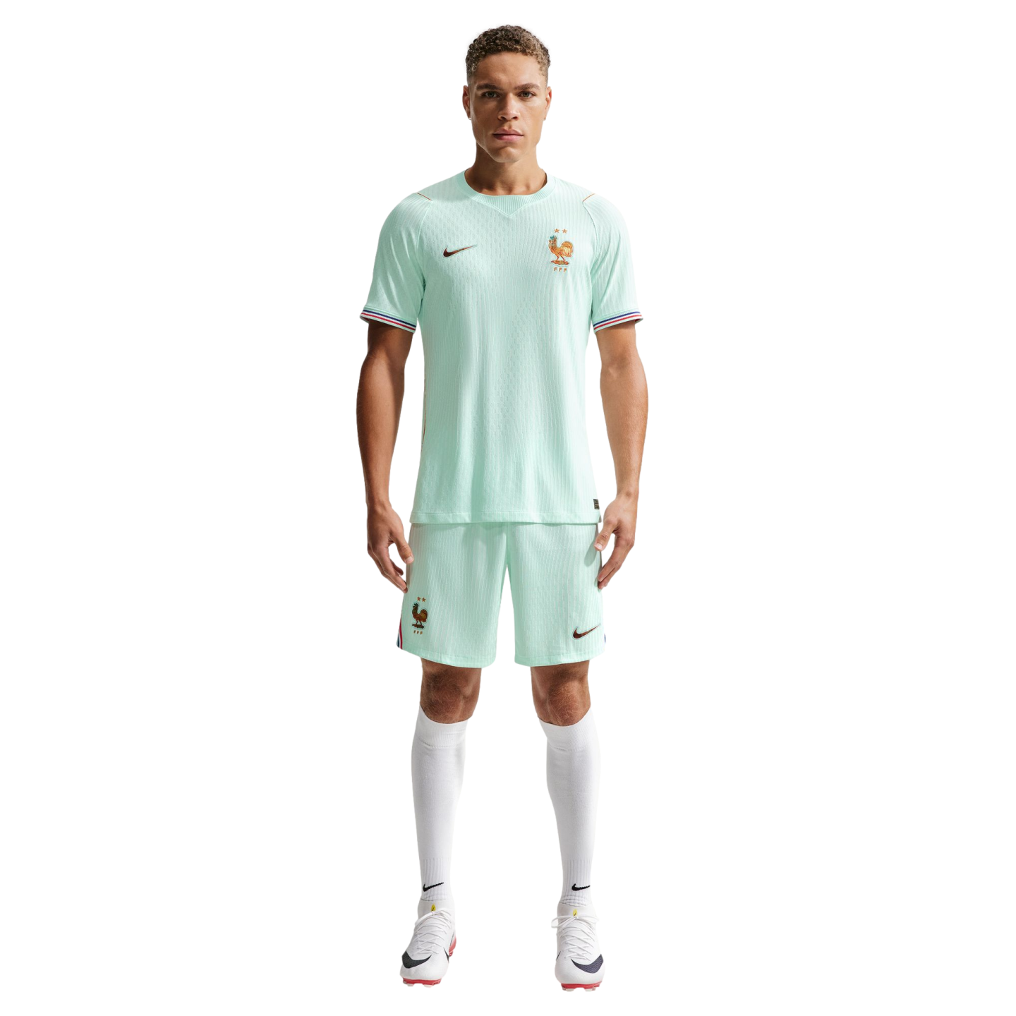 A man models a light mint green Nike France soccer kit with white socks and cleats against a black background.
