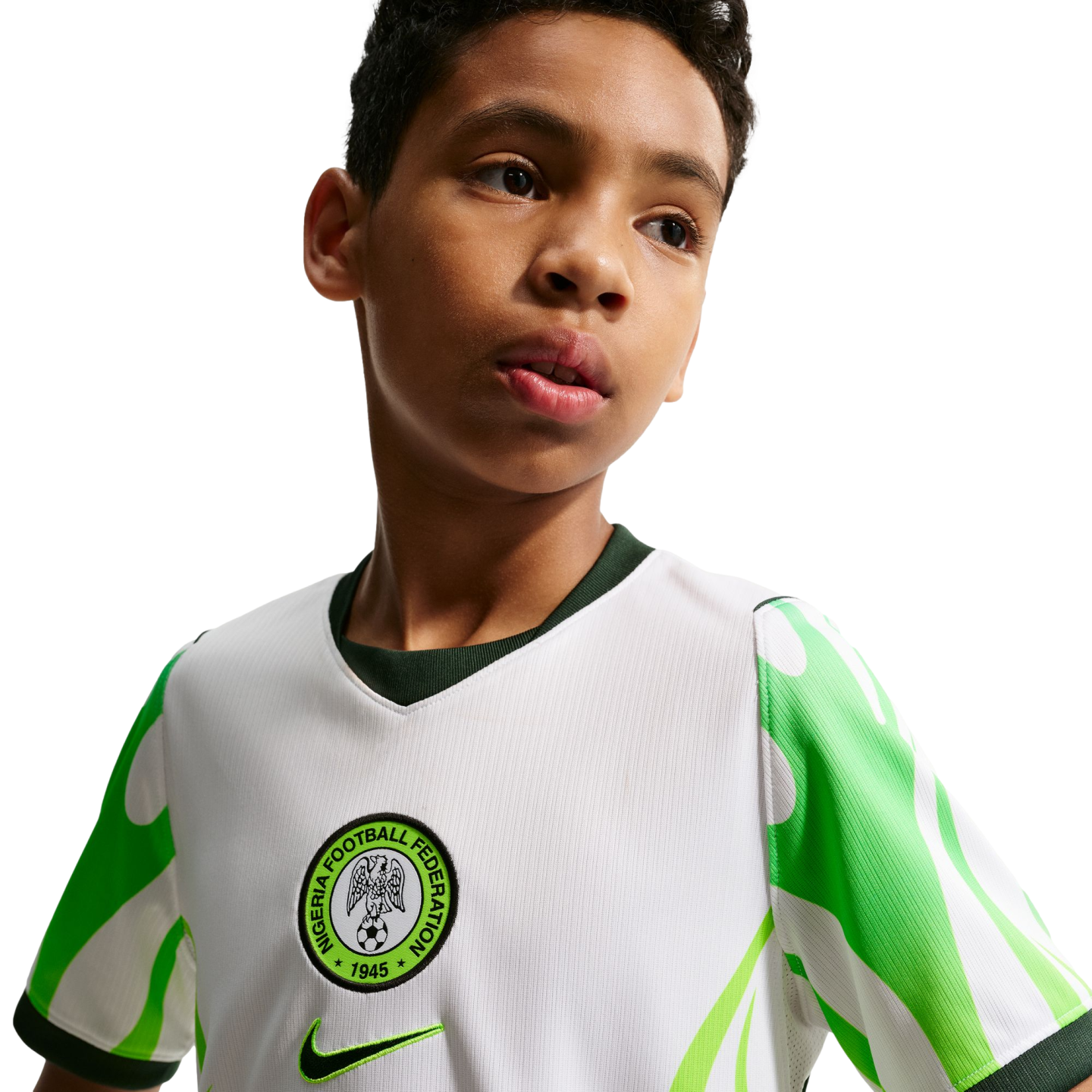 A young boy looking off-camera, wearing a white Nigeria national football team jersey with green patterned sleeves and the federation's crest.