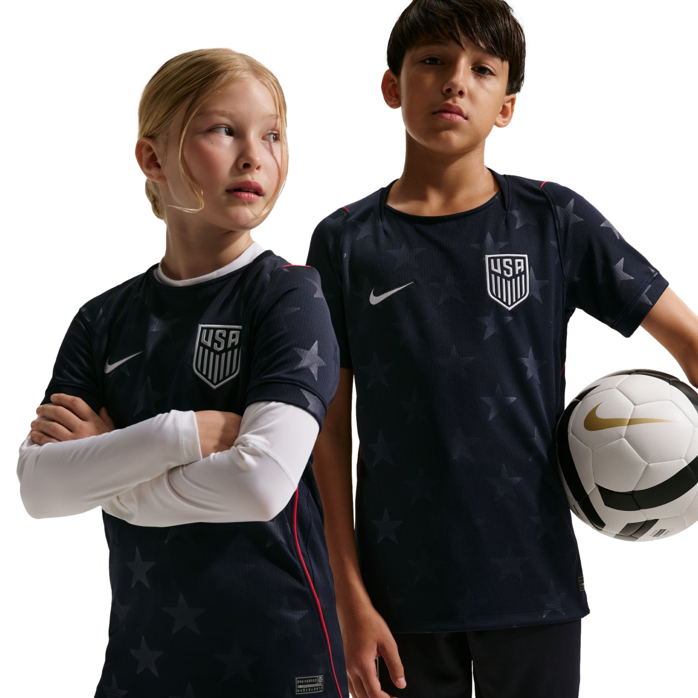 A girl and boy wear navy blue star-patterned USA soccer jerseys; the boy holds a soccer ball. Black background.