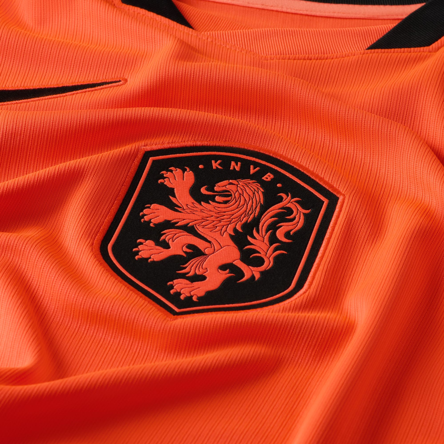 A close-up of a bright orange textured soccer jersey featuring the black KNVB shield crest with an orange lion rampant.