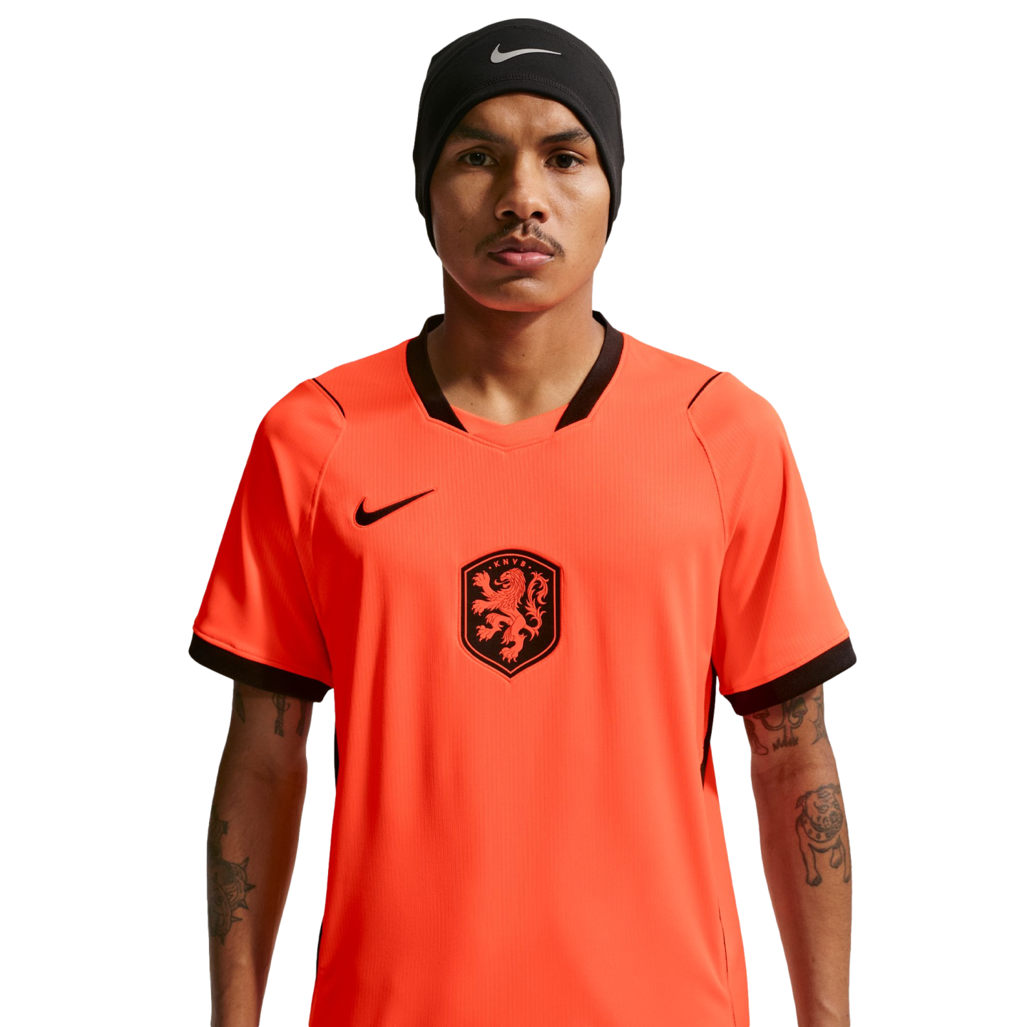 A man wearing a bright orange Netherlands national football team jersey and a black Nike beanie, centered against a solid black background. He has a mustache and visible tattoos on his arms.