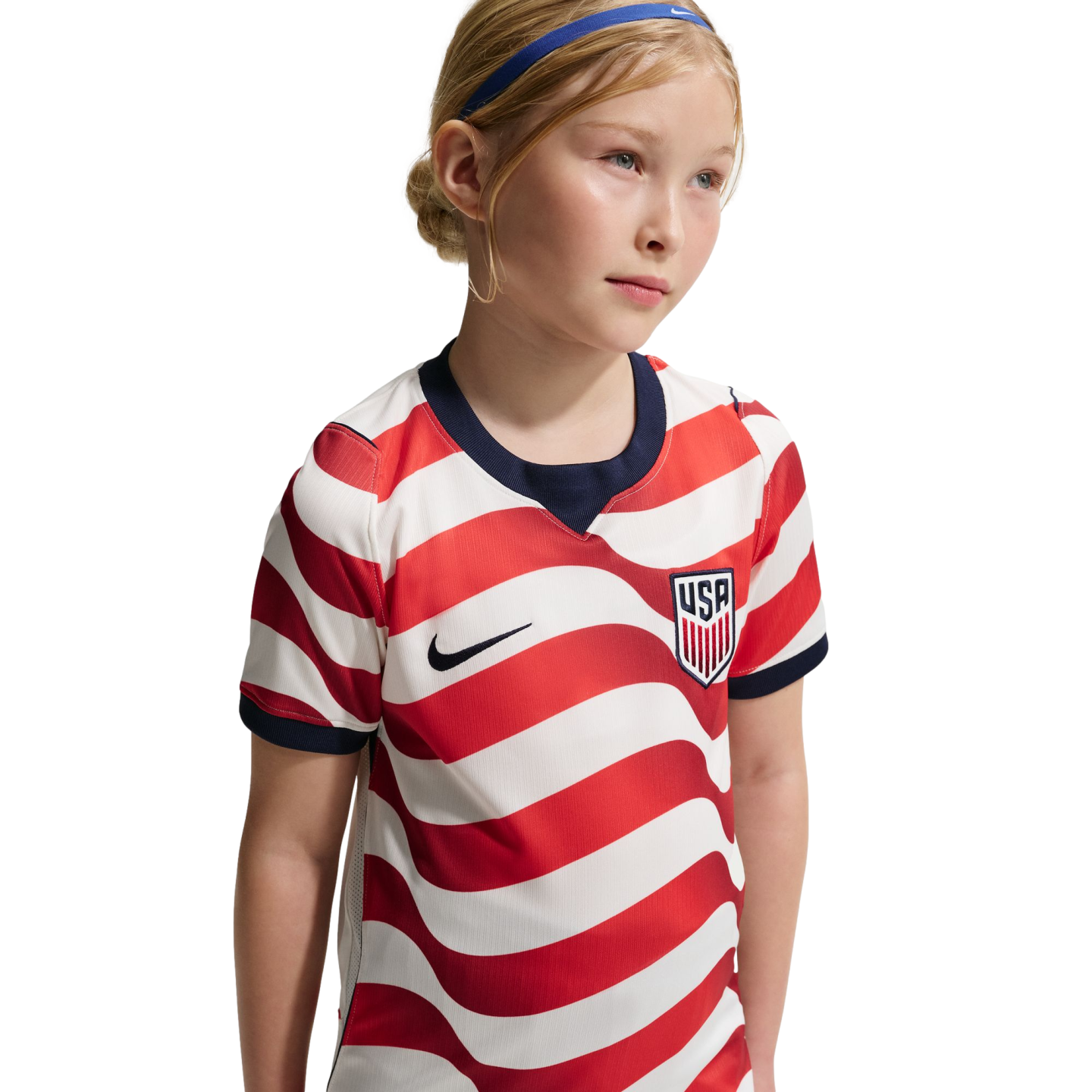A young girl in a red and white striped USA soccer jersey and blue headband, set against a black background.