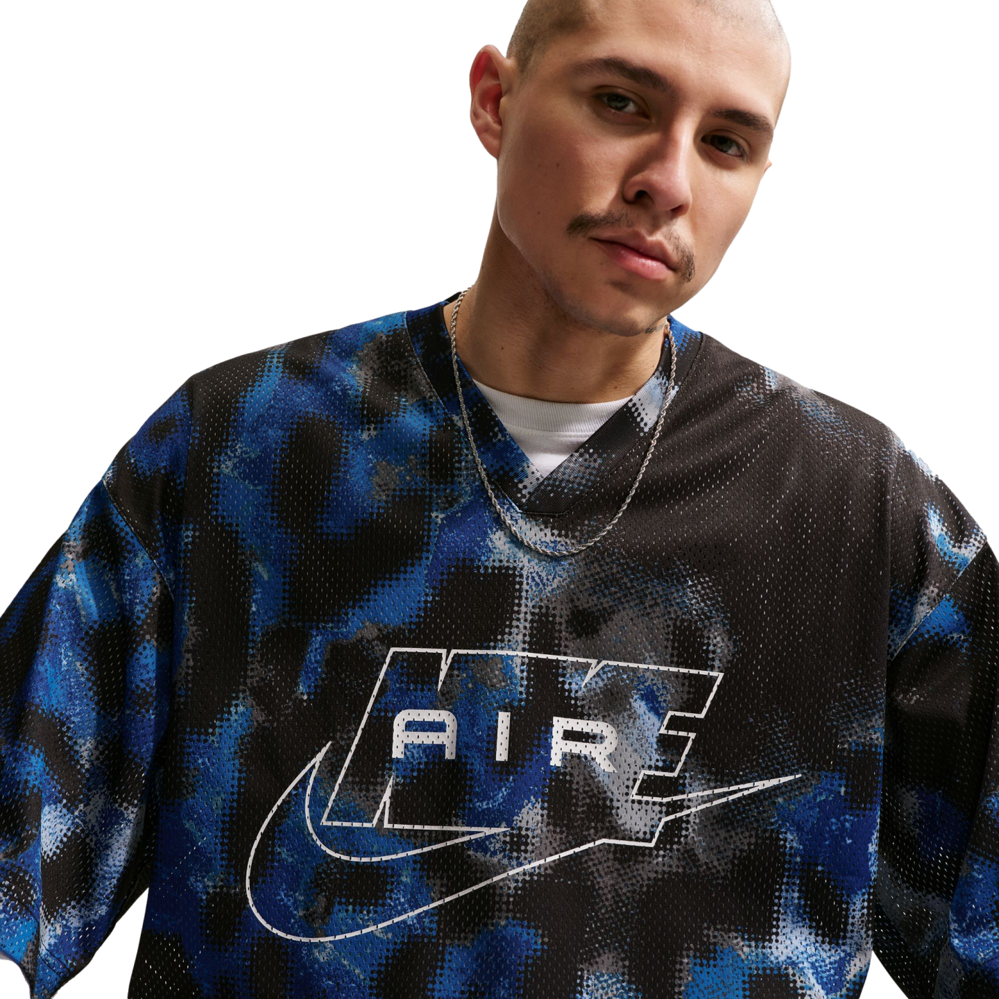 A person with a shaved head wears a blue and black patterned mesh Nike "AIR" jersey and a silver chain against a white background.
