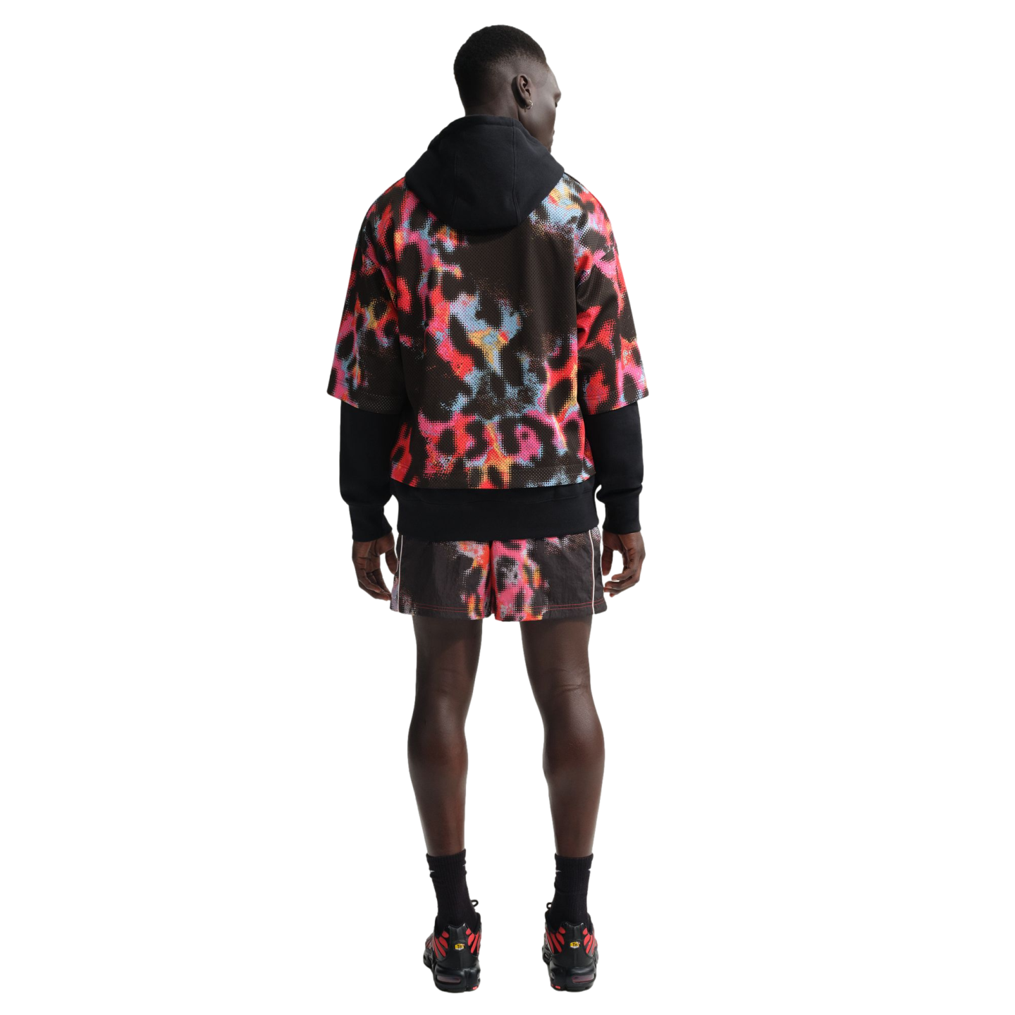 Rear view of a man wearing a black hoodie under a colorful abstract-print mesh jersey with matching shorts, black socks, and sneakers on a white background.
