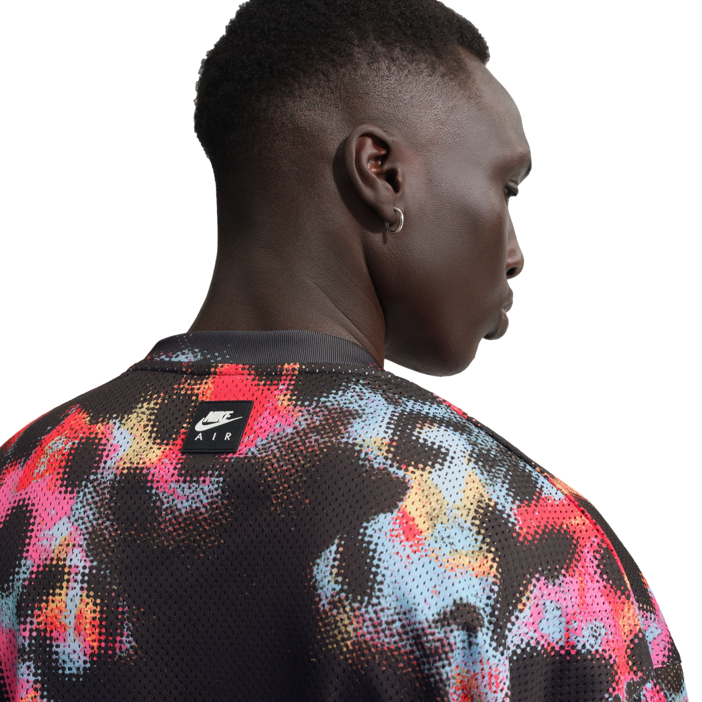 A close-up, back-profile view of a person wearing a black mesh Nike Air shirt with a vibrant red, blue, and pink abstract paint-splatter pattern.