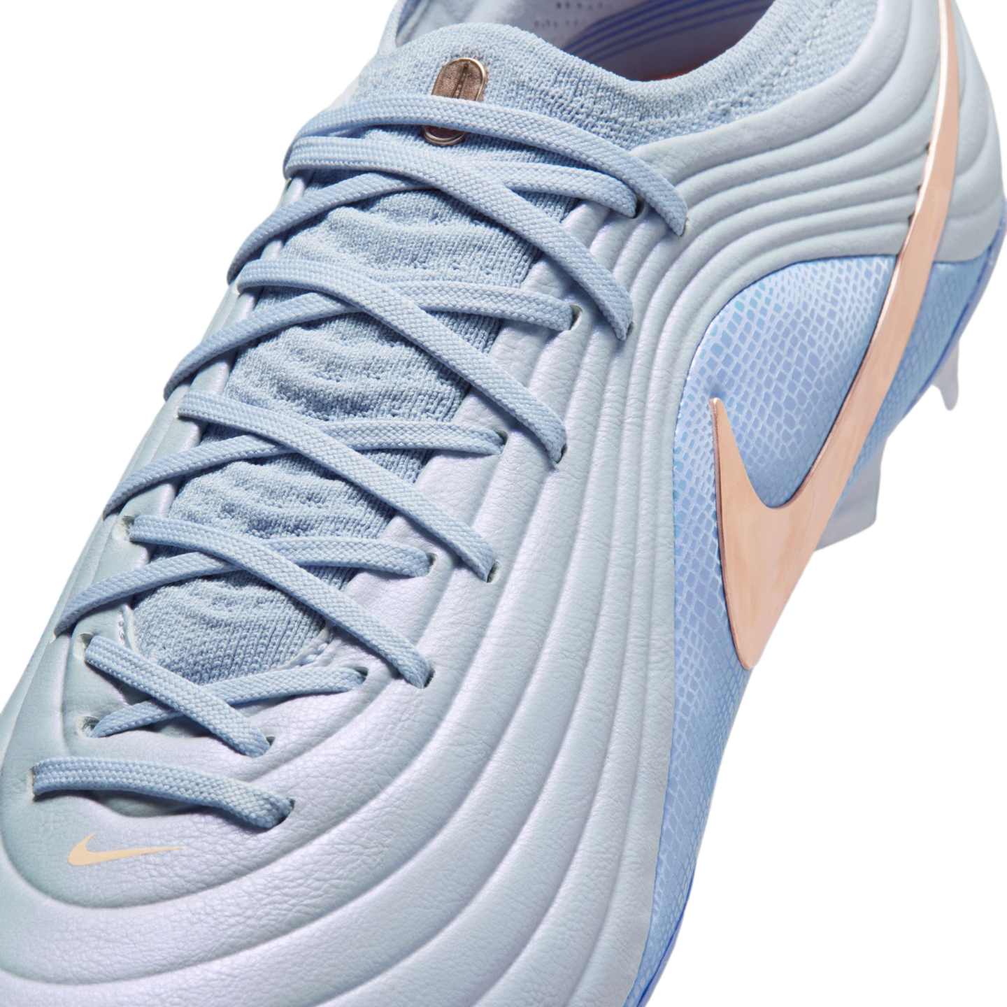 Close-up of a light blue Nike soccer cleat featuring a textured wavy upper, a rose gold Swoosh, and light blue laces against a black background.