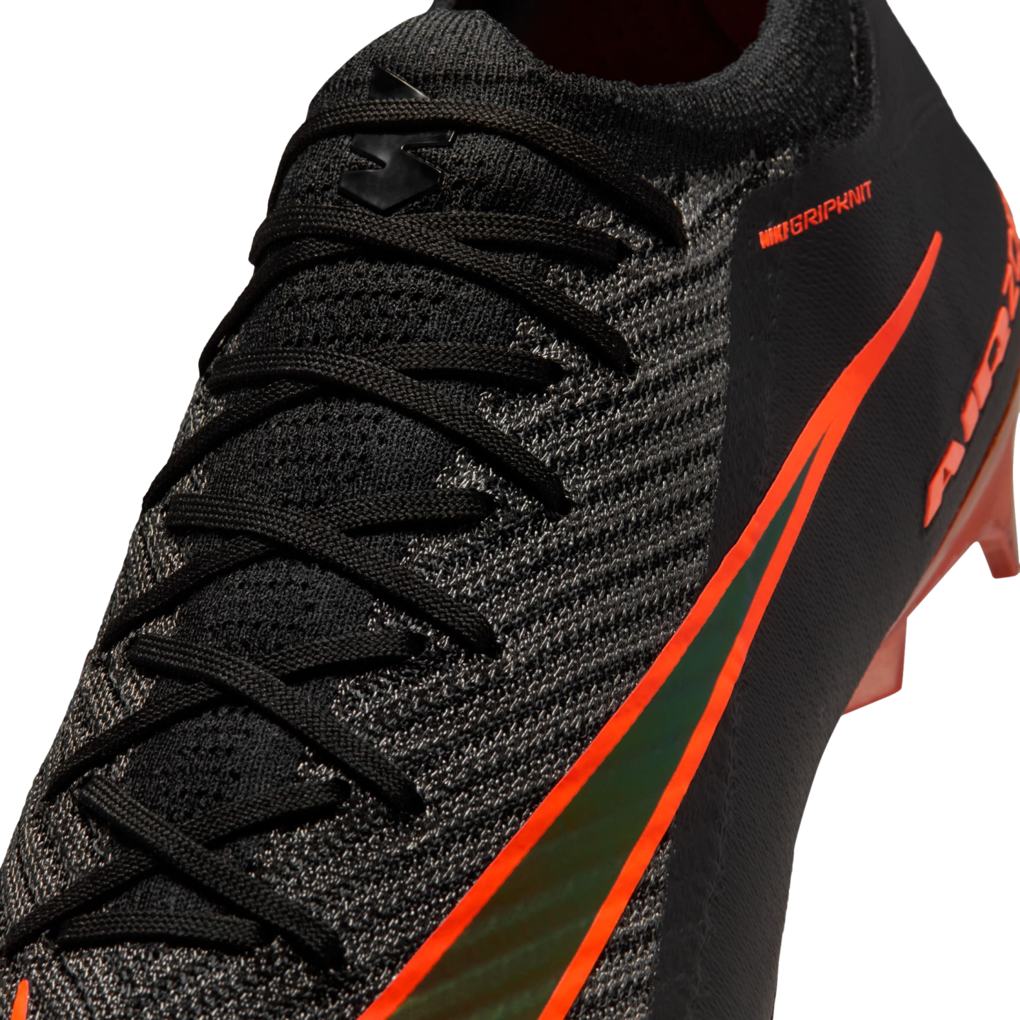 Close-up of a black Nike soccer boot featuring textured Gripknit, black laces, and a vibrant orange swoosh with an iridescent center.