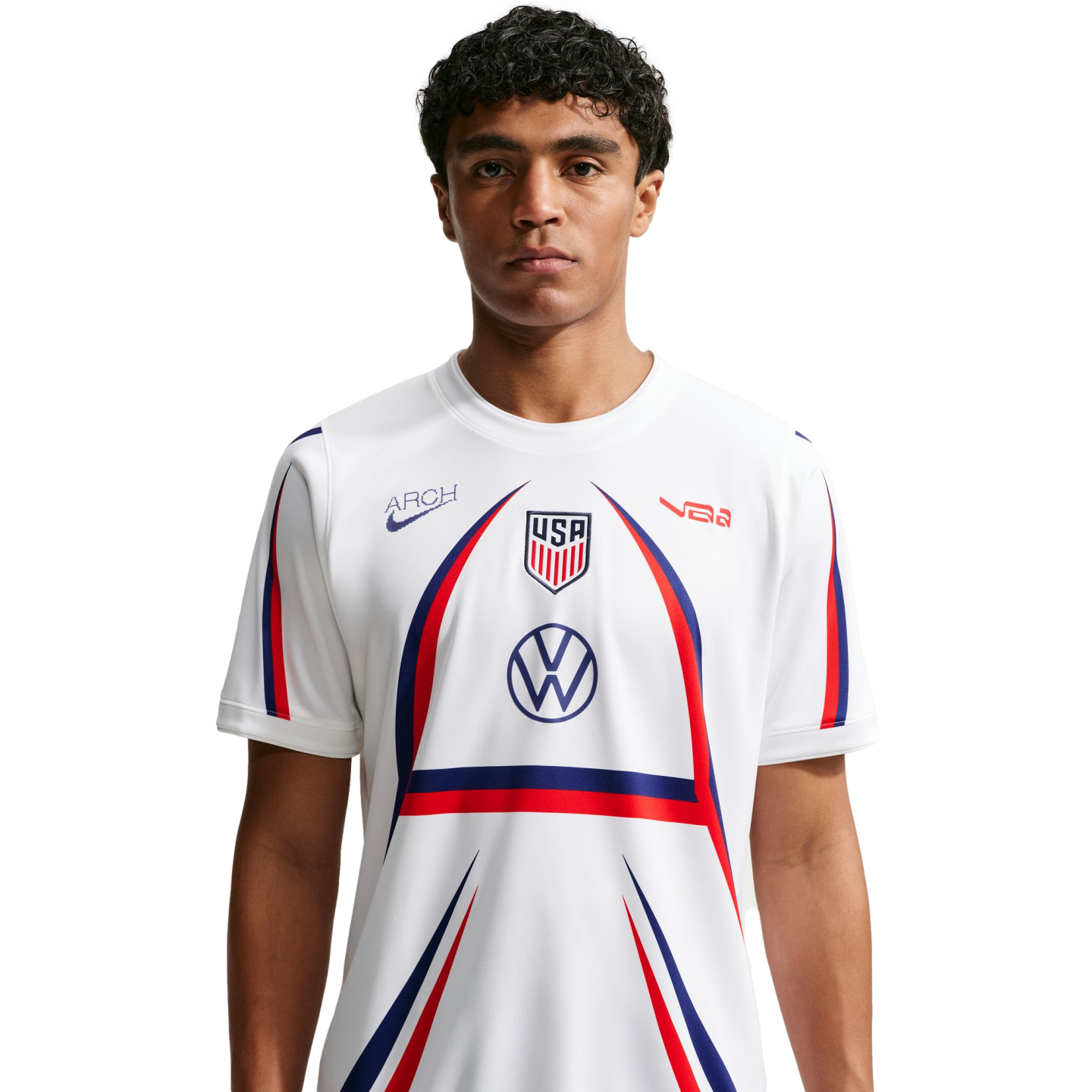 A man with curly hair wears a white USA soccer jersey featuring red and blue accents and a large arch design, centered against a plain white background.