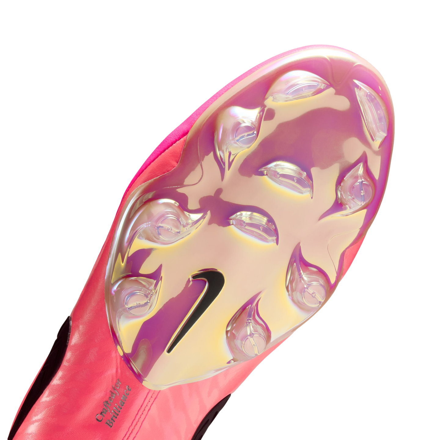 Bottom of a pink Nike soccer cleat featuring an iridescent soleplate, clear studs, a black Nike swoosh, and the text "Crafted for Brilliance" near the heel.