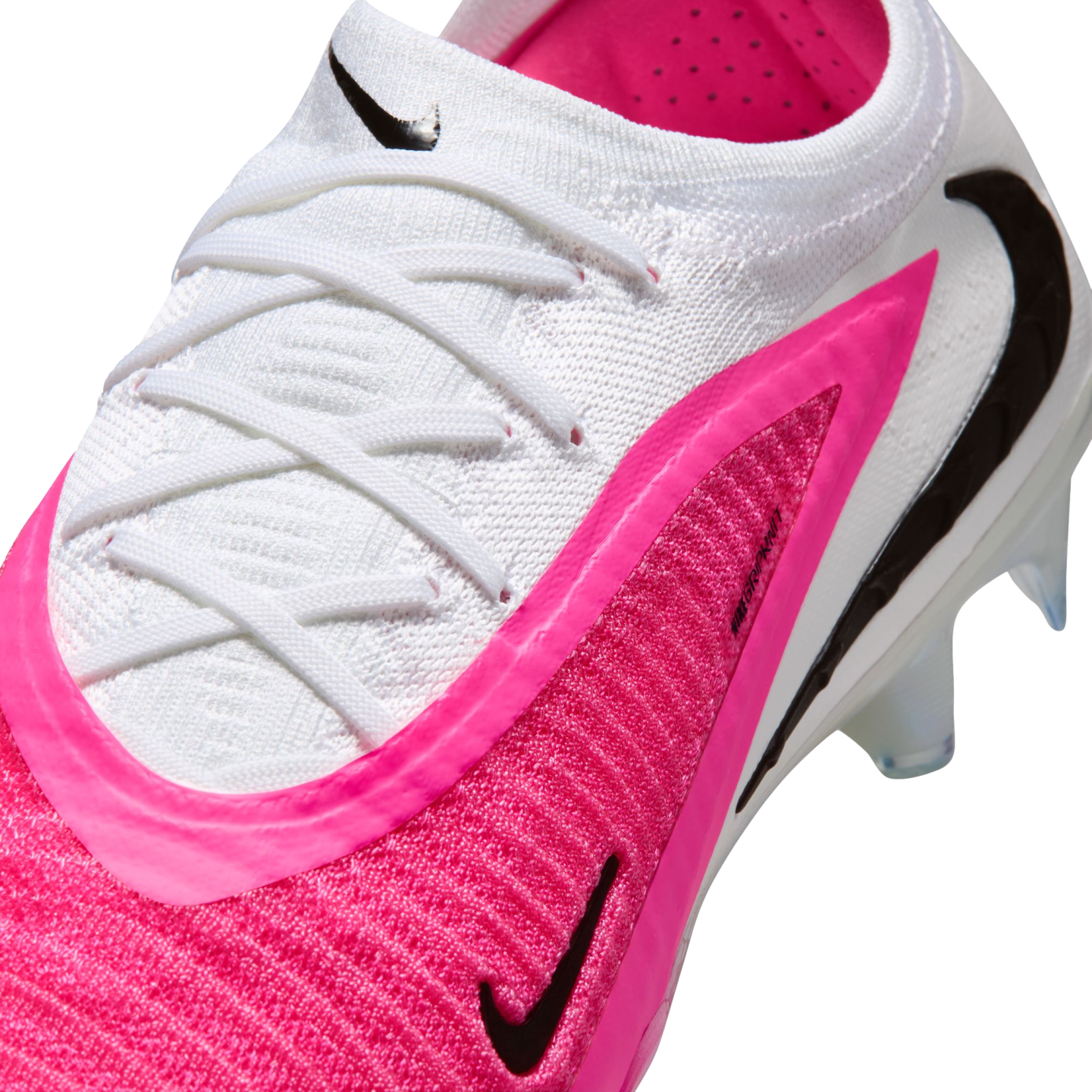 A close-up of a white and bright pink Nike soccer cleat with black swooshes, white laces, and textured Gripknit material.
