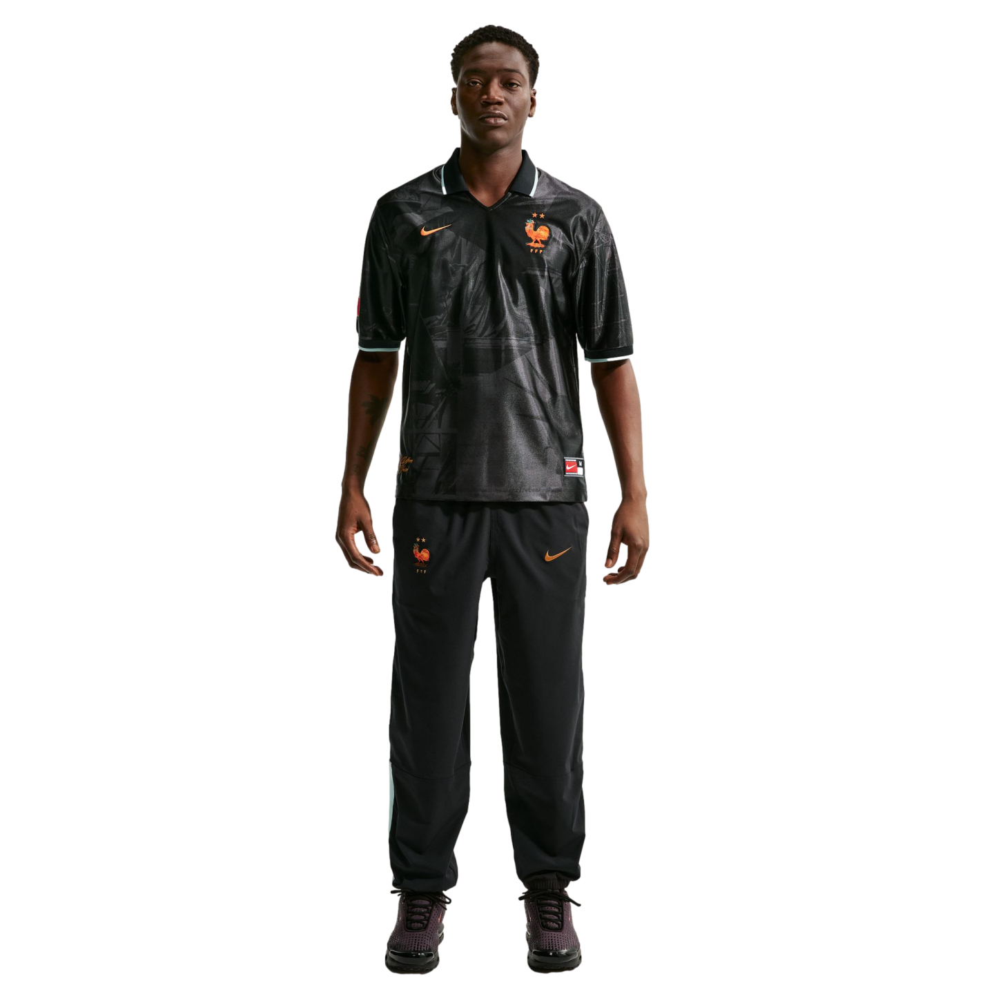 Full-length photo of a man in a black Nike France training kit with orange details, standing against a white background.