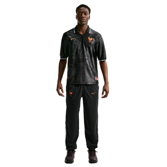 Full-length photo of a man in a black Nike France training kit with orange details, standing against a white background.