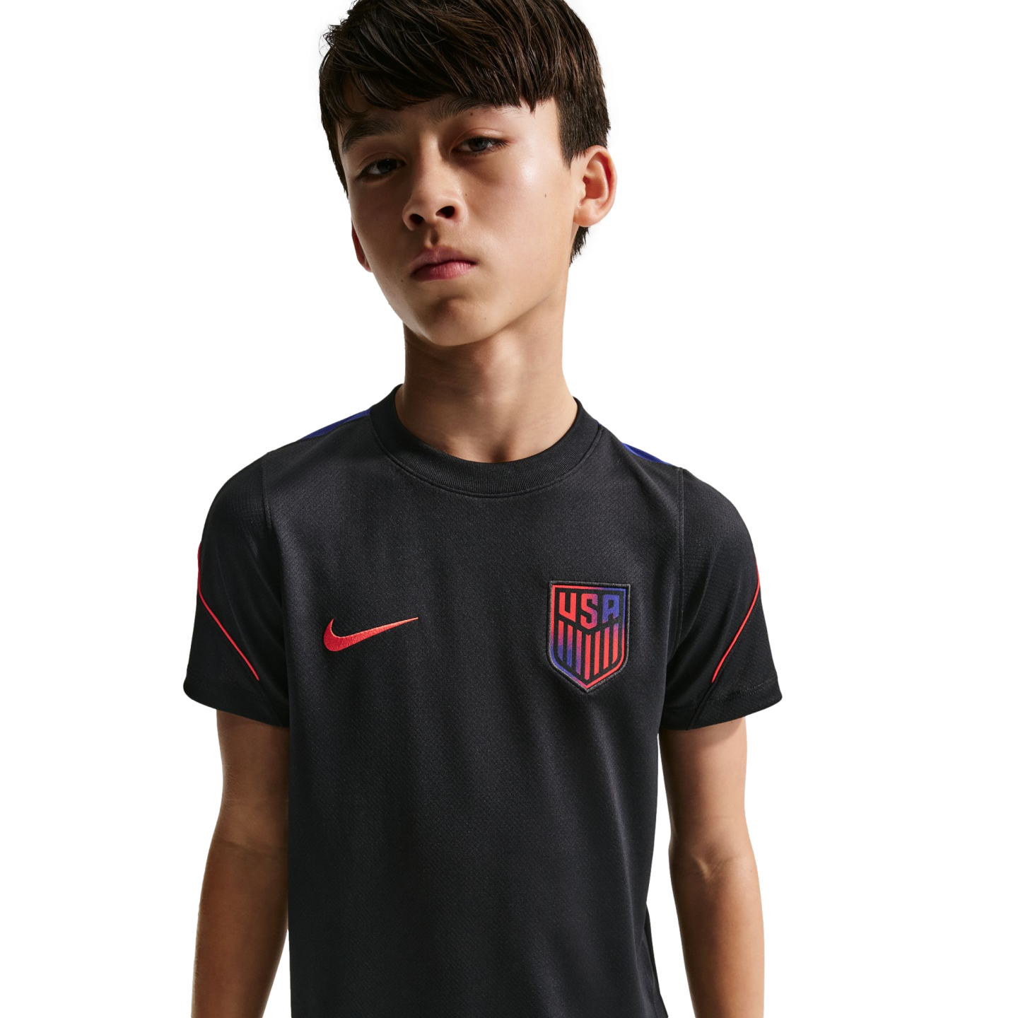 A young boy with short brown hair wearing a black Nike USA soccer jersey, looking at the camera against a solid black background.