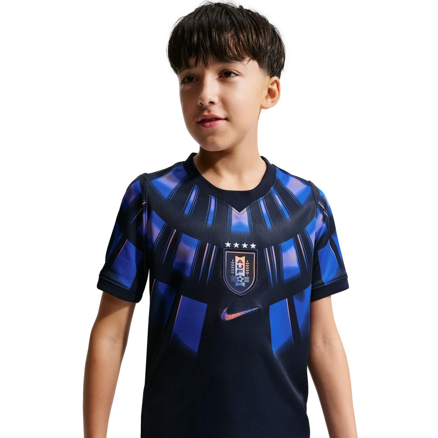 A young boy wearing a navy blue Uruguay national team soccer jersey with iridescent blue and purple patterns. The jersey features the AUF crest on the chest and a Nike swoosh logo, set against a solid black background.