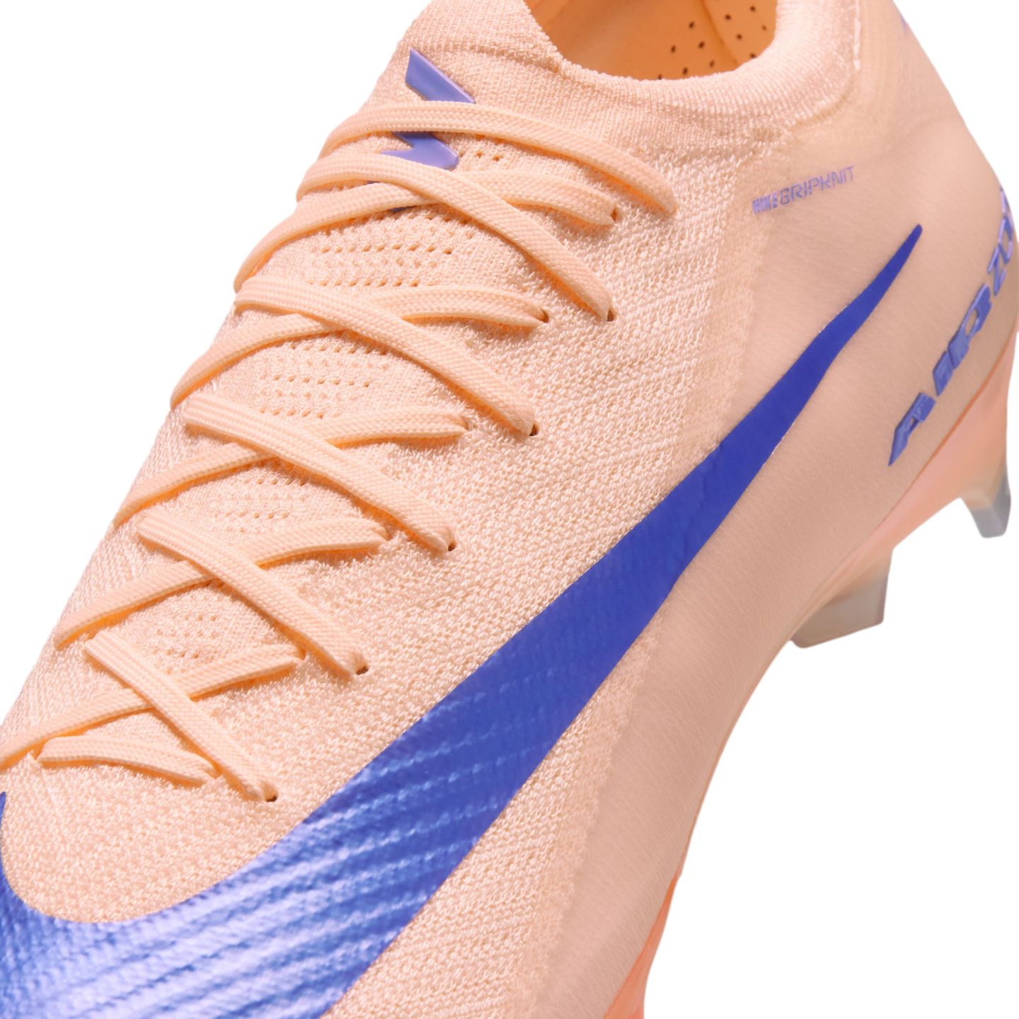 Close-up of a peach-colored Nike soccer cleat with a blue swoosh and a textured knit upper.