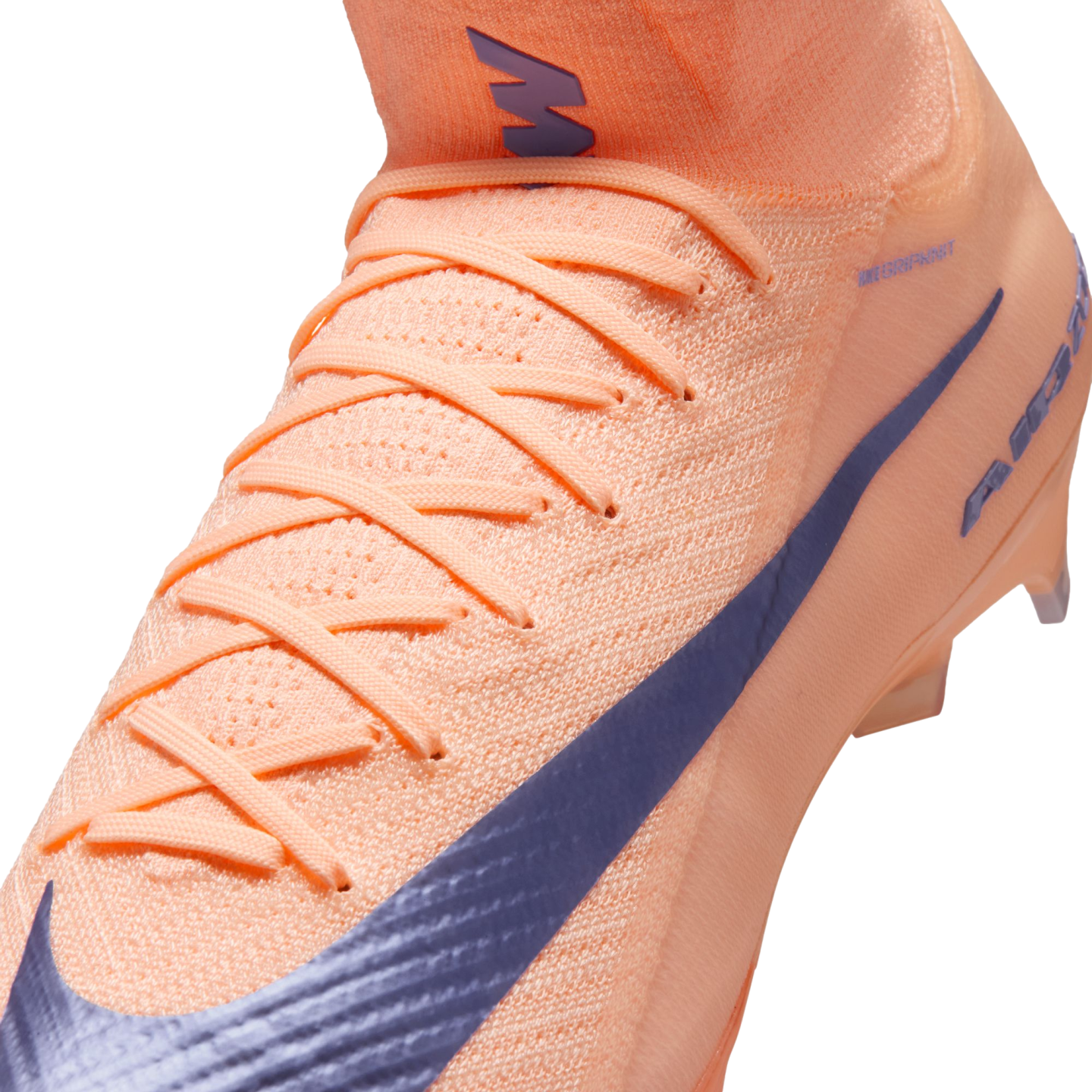 Close-up of a peach-colored Nike soccer cleat featuring a textured knit upper, matching laces, and a large purple swoosh.