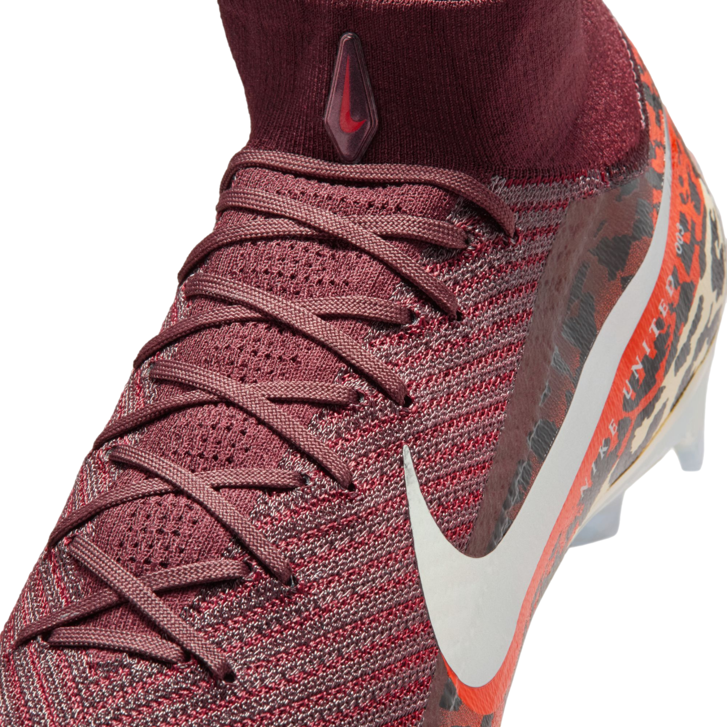 A close-up, high-angle shot shows a maroon Nike soccer cleat against a black background. The shoe features a textured, knit upper with maroon laces and a high-top sock collar. A small, teardrop-shaped logo with a red swoosh is on the front of the collar, 