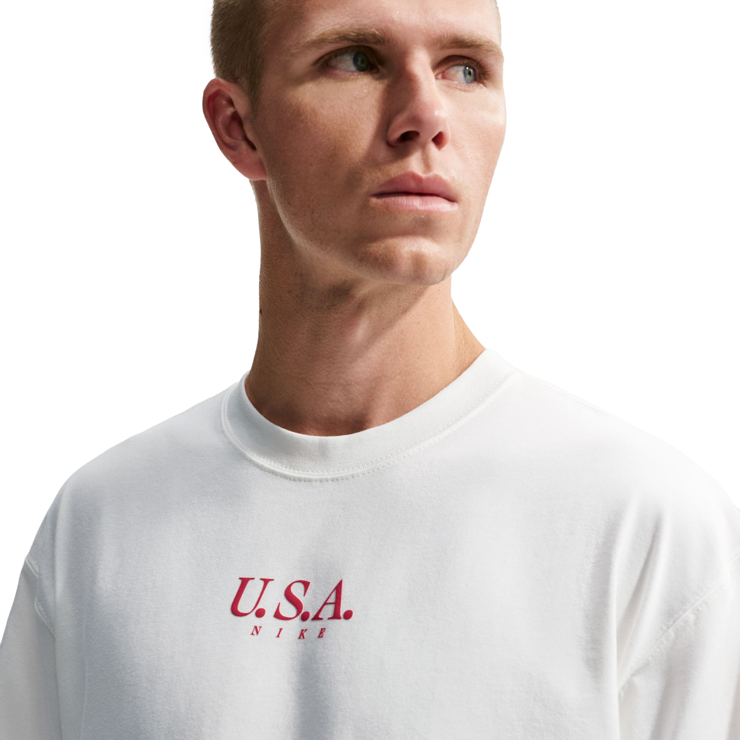 A man in a white Nike crewneck t-shirt with red "U.S.A. NIKE" text on the chest, looking off to the side against a solid black background.
