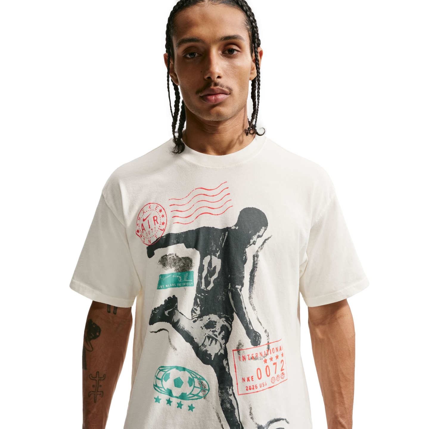 A young man with braided hair and a thin mustache wearing a cream-colored T-shirt with a large soccer-themed graphic, set against a solid black background.