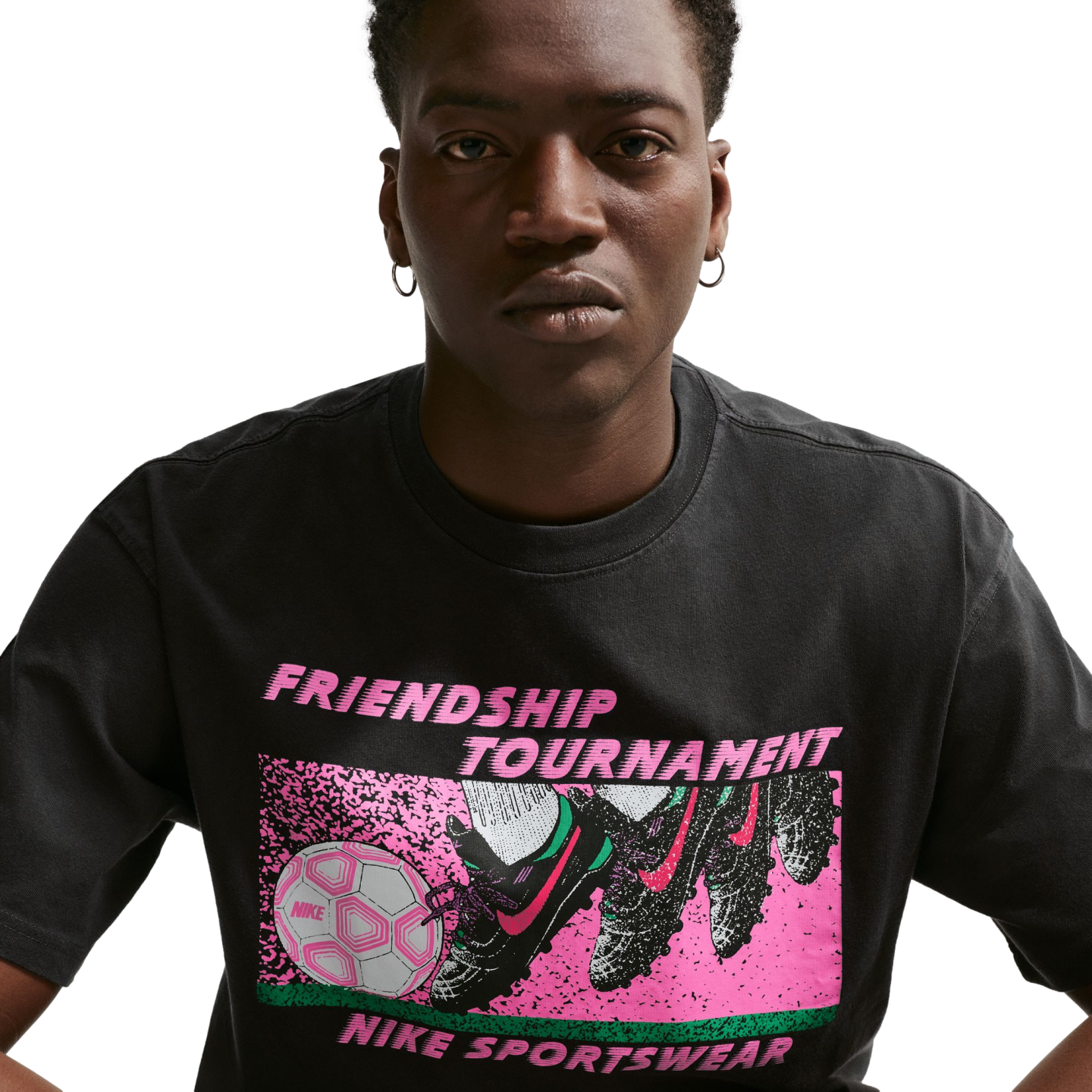 A person wearing a black Nike t-shirt with a pink and green "FRIENDSHIP TOURNAMENT" soccer graphic on the front.