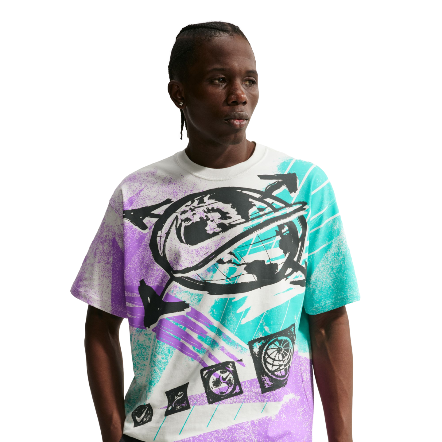 A young Black man with braided hair poses against a solid black background, wearing a white Nike t-shirt with a large, vibrant graphic. The shirt's central design features a black globe with a Nike swoosh wrapped around it, surrounded by bold, textured sp