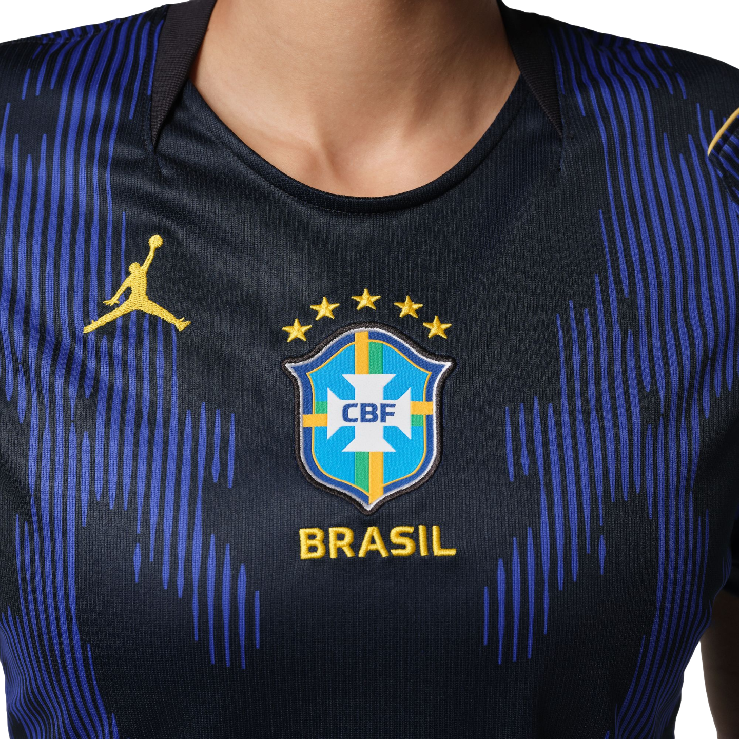 Close-up of a dark blue Brazil football jersey featuring vertical stripes, the CBF crest with five stars, and a yellow Jordan Jumpman logo.